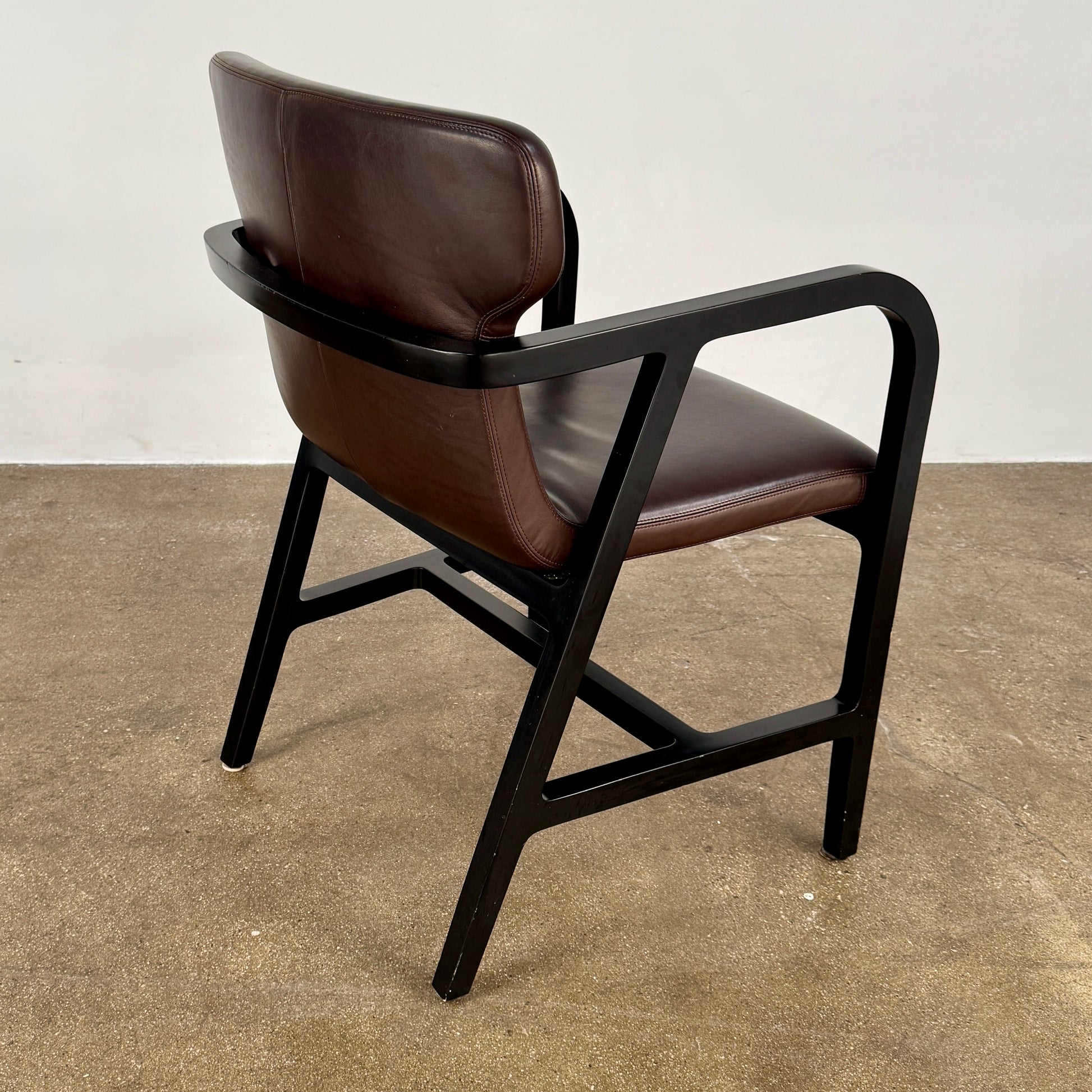 A pair of Maxalto Fulgens Armchair set (2) by Maxalto, in dark brown leather with black wooden frames, are placed side by side against a plain white background.