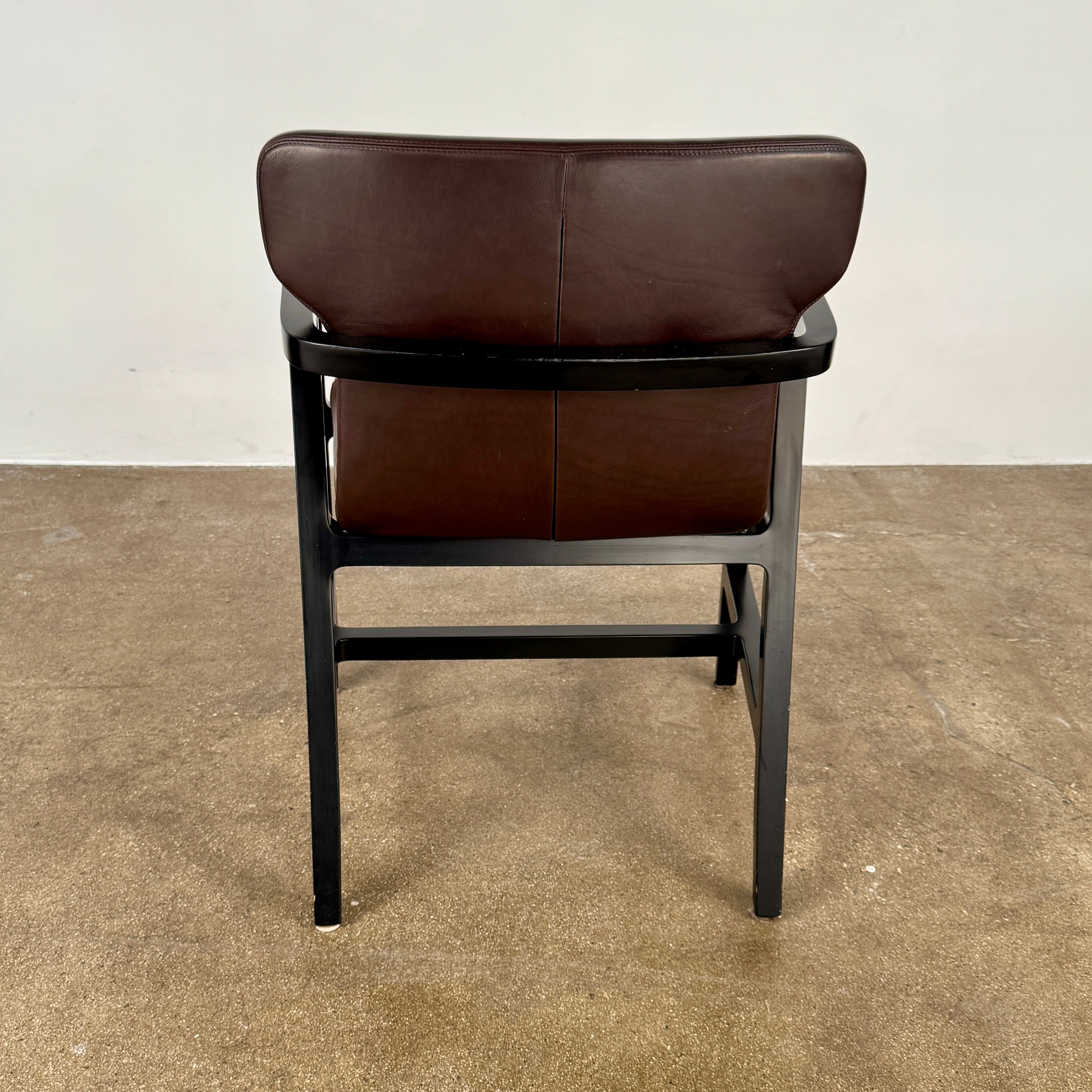 A pair of Maxalto Fulgens Armchair set (2) by Maxalto, in dark brown leather with black wooden frames, are placed side by side against a plain white background.