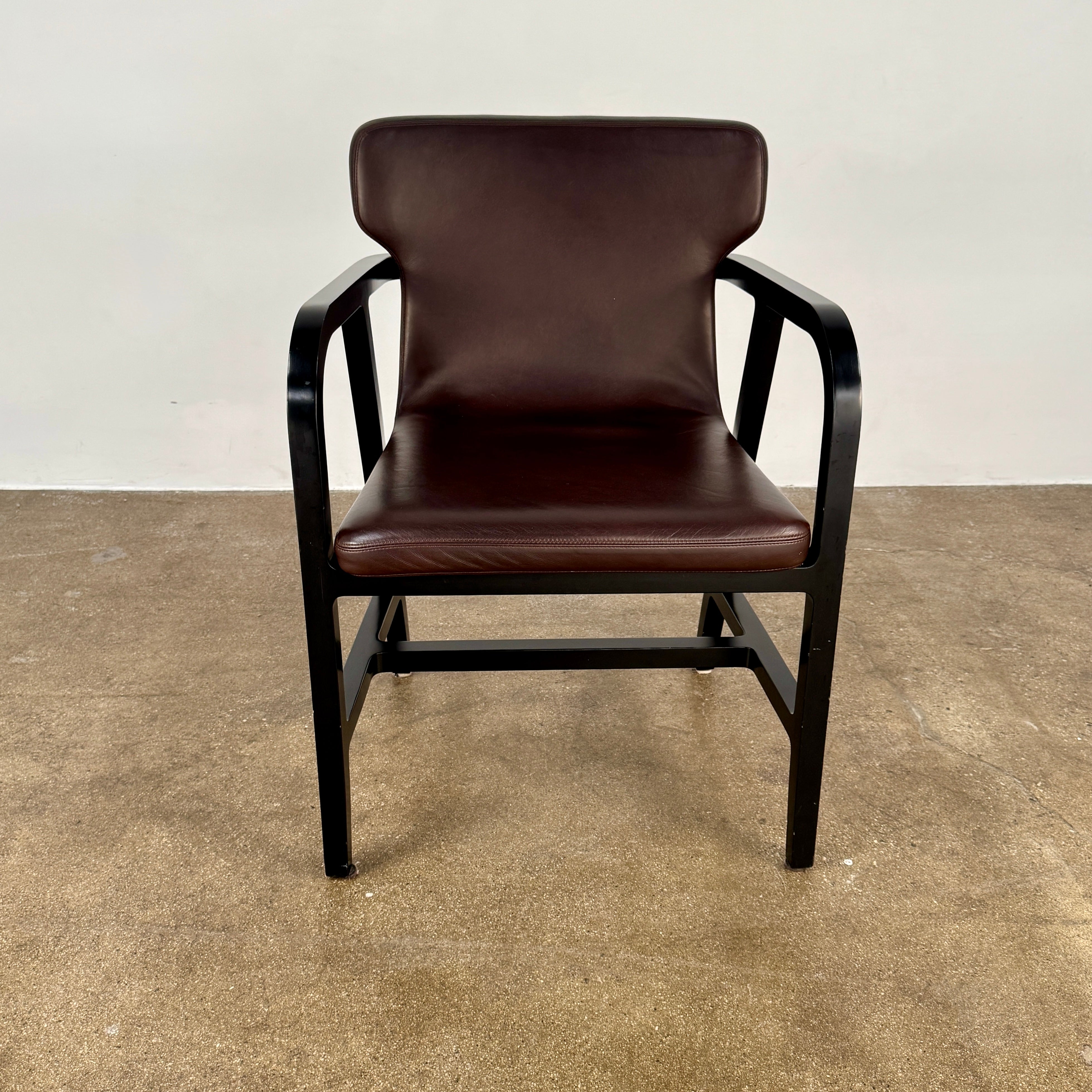 A pair of Maxalto Fulgens Armchair set (2) by Maxalto, in dark brown leather with black wooden frames, are placed side by side against a plain white background.