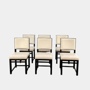 A Maxalto Teti Dining Chair from a set of 6, featuring a black frame with white upholstered seat and backrest, stands on a brown concrete floor against a plain light gray wall.