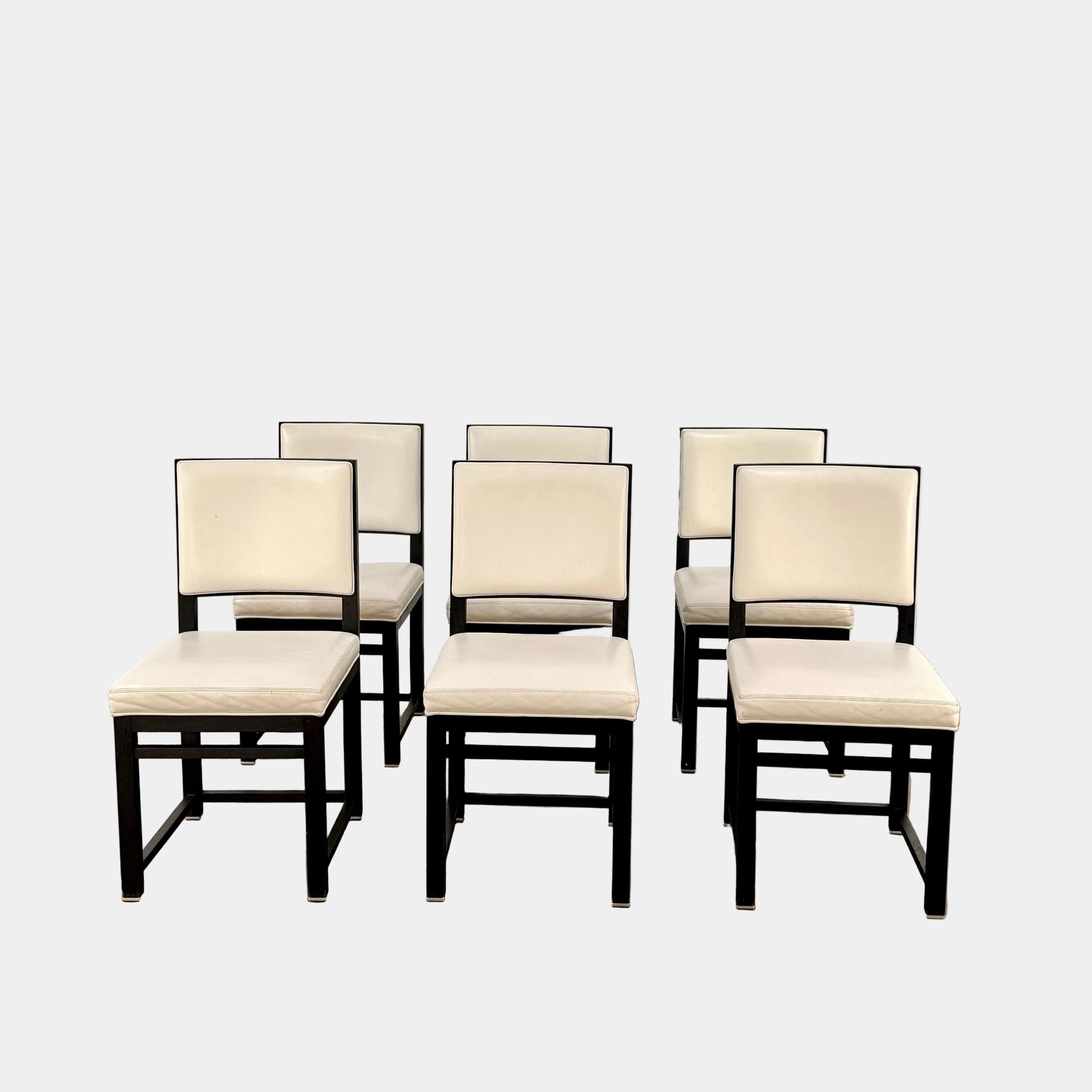 A Maxalto Teti Dining Chair from a set of 6, featuring a black frame with white upholstered seat and backrest, stands on a brown concrete floor against a plain light gray wall.