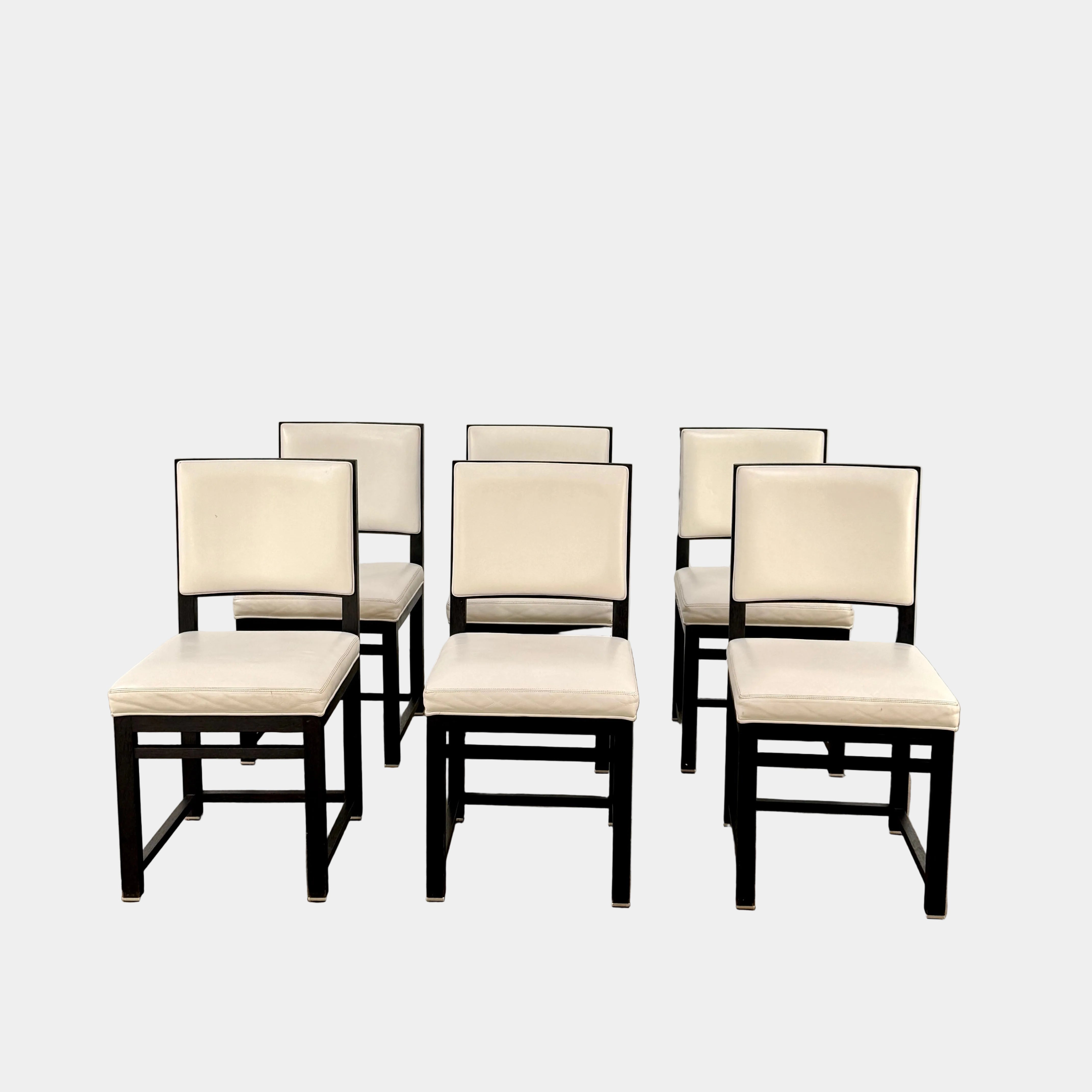 A Maxalto Teti Dining Chair from a set of 6, featuring a black frame with white upholstered seat and backrest, stands on a brown concrete floor against a plain light gray wall.