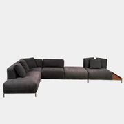 The Cassina Mex Hi Modular Sofa by Cassina features dark gray recycled fiber upholstery, metal legs, multiple cushions, and an integrated wooden side table, shown against a white background.