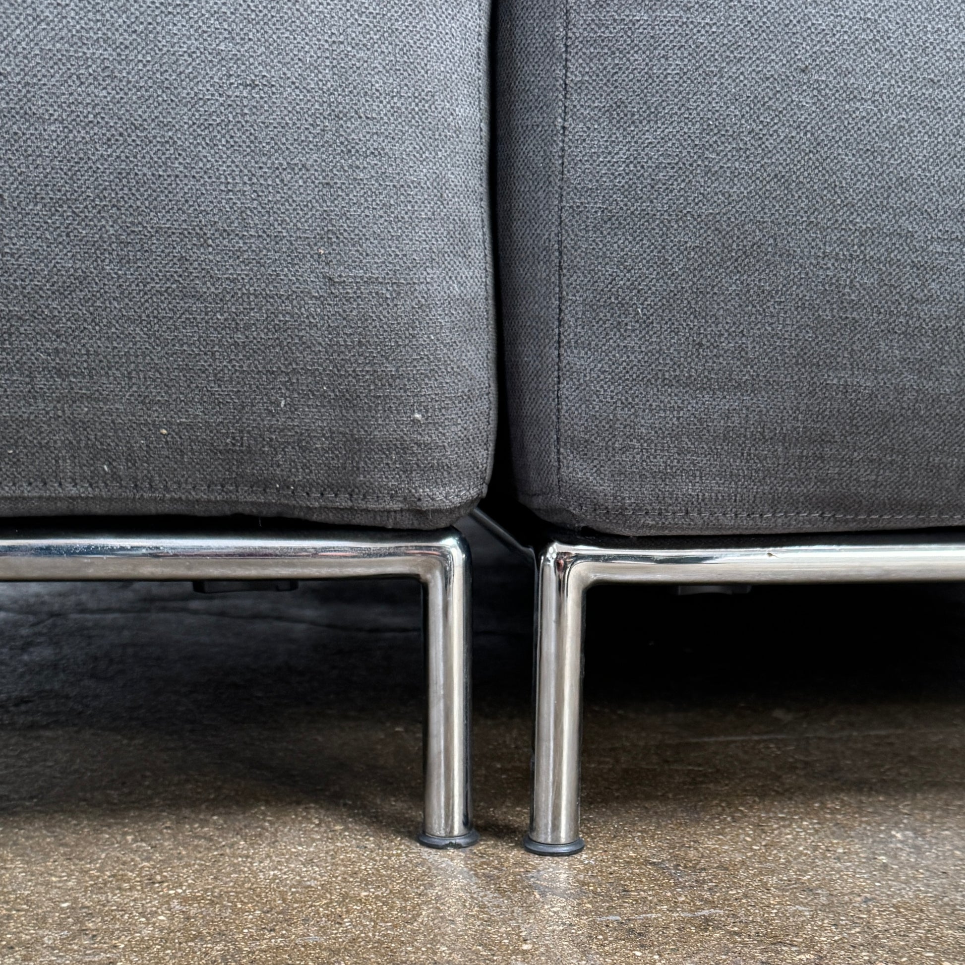 The Cassina Mex Hi Modular Sofa by Cassina features dark gray recycled fiber upholstery, metal legs, multiple cushions, and an integrated wooden side table, shown against a white background.