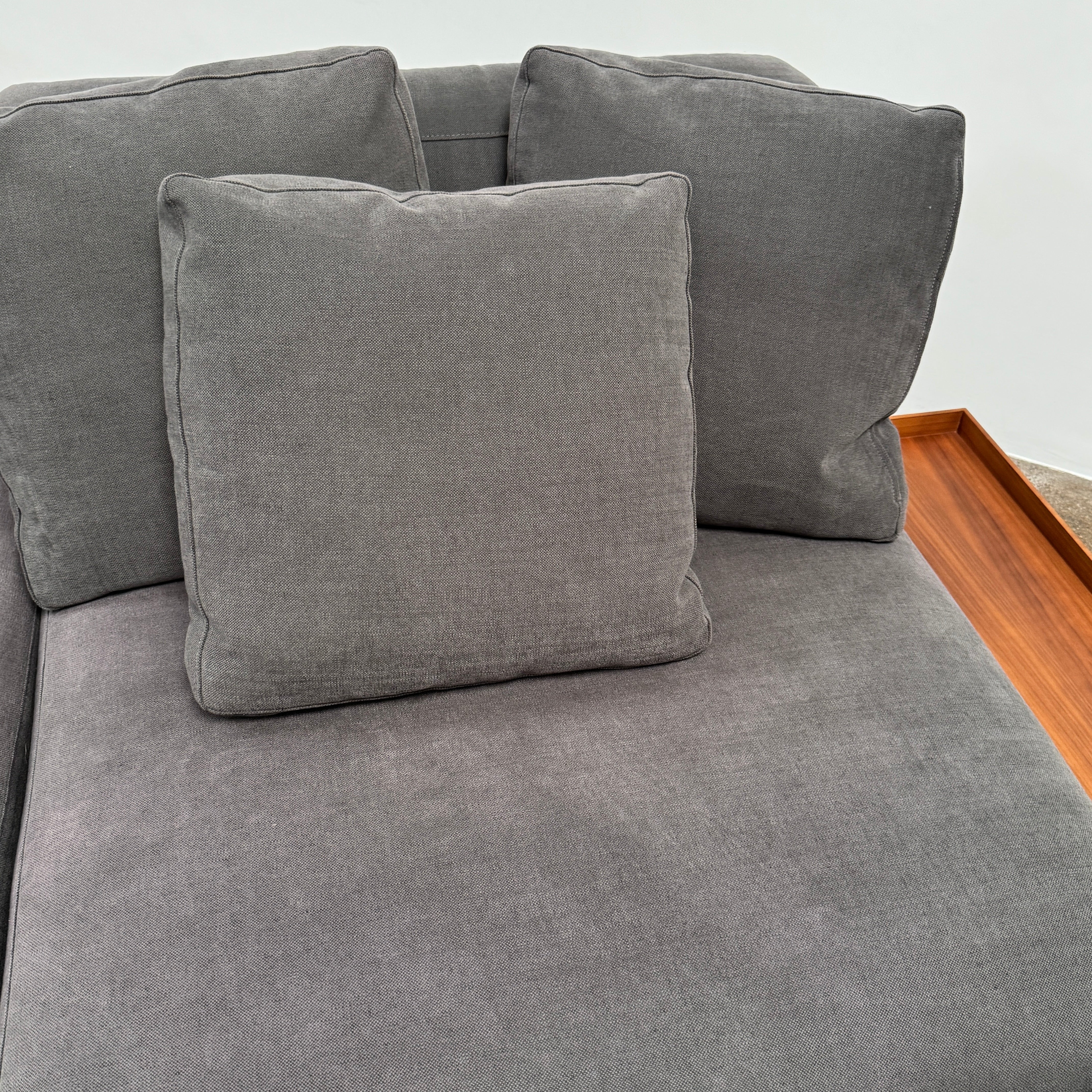 The Cassina Mex Hi Modular Sofa by Cassina features dark gray recycled fiber upholstery, metal legs, multiple cushions, and an integrated wooden side table, shown against a white background.