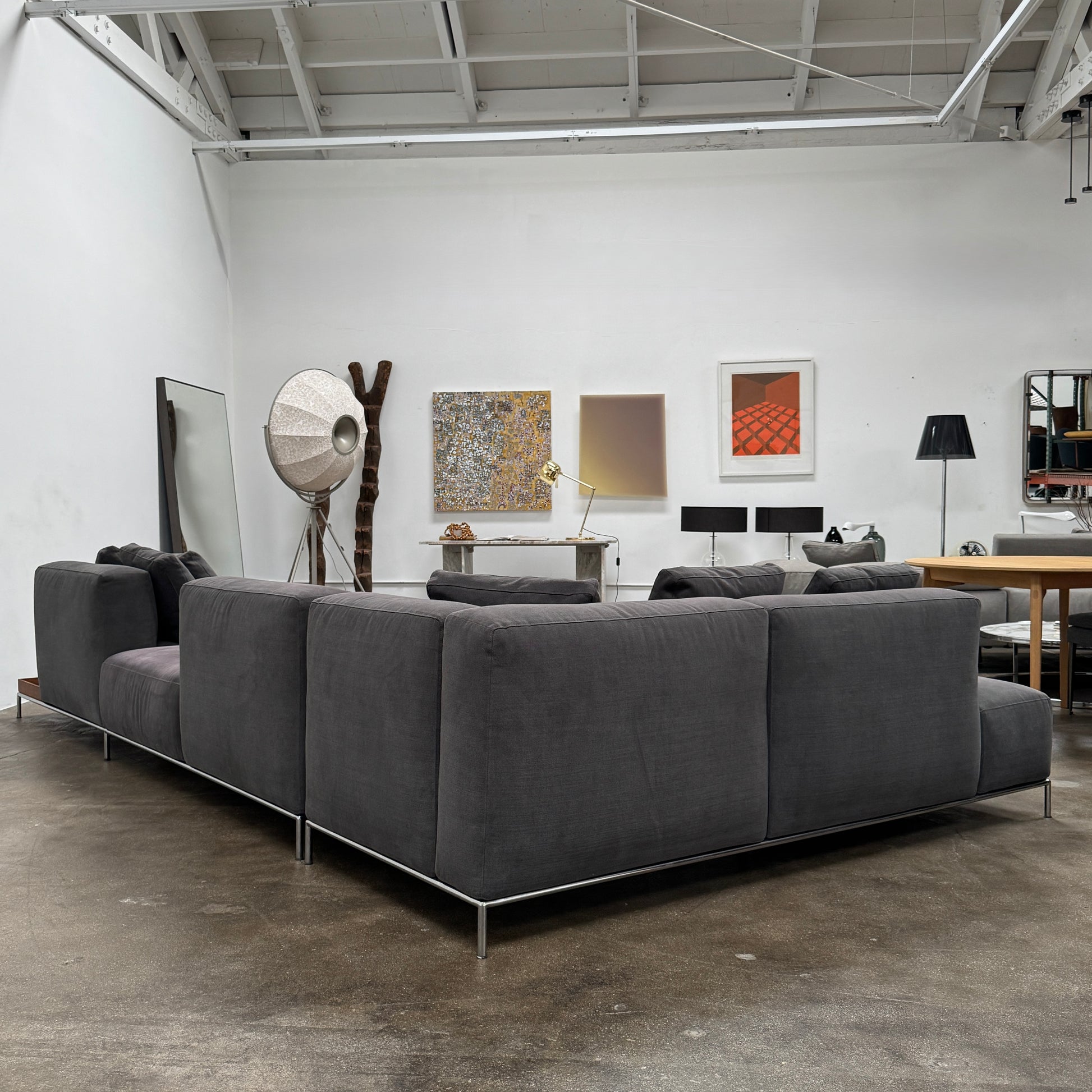 The Cassina Mex Hi Modular Sofa by Cassina features dark gray recycled fiber upholstery, metal legs, multiple cushions, and an integrated wooden side table, shown against a white background.