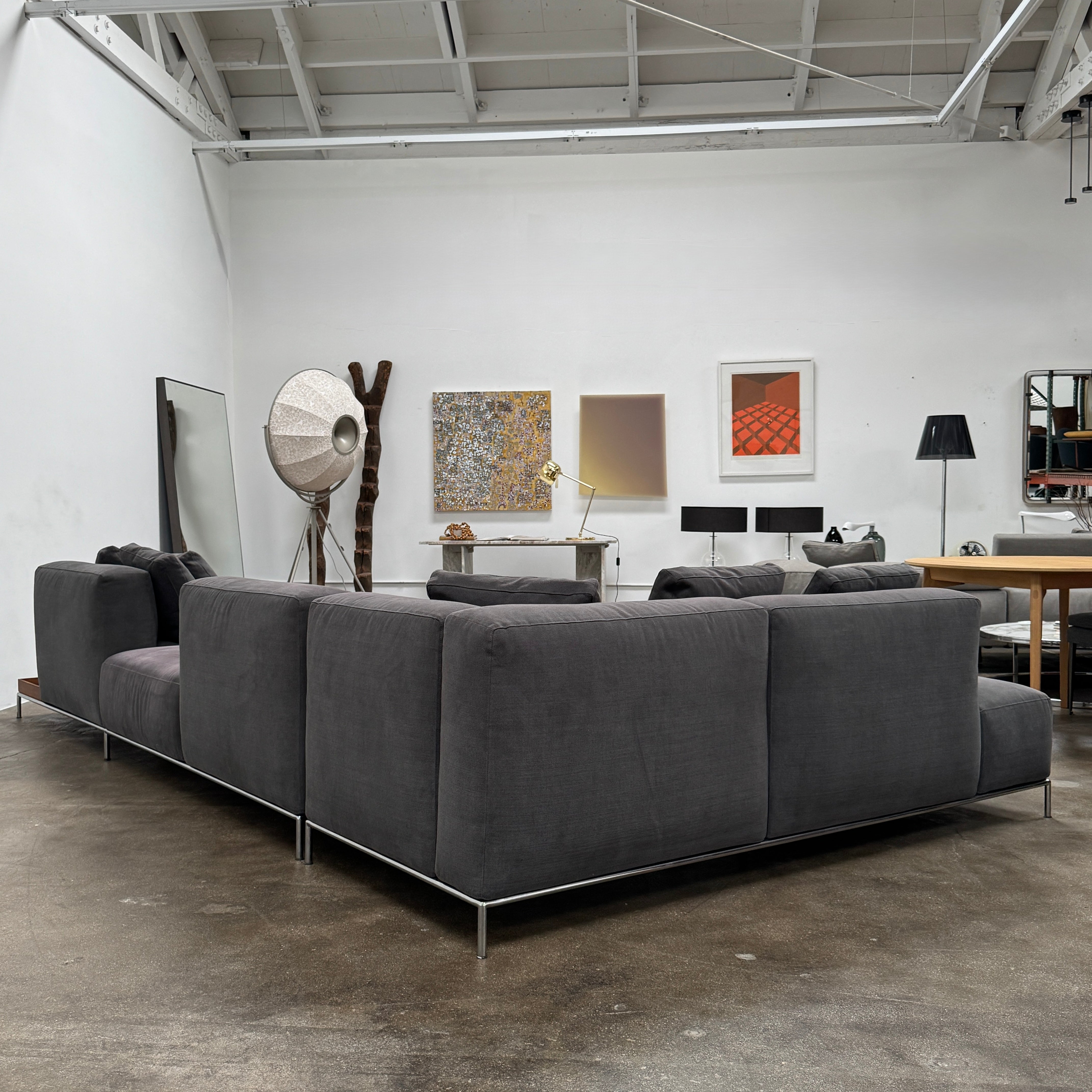 The Cassina Mex Hi Modular Sofa by Cassina features dark gray recycled fiber upholstery, metal legs, multiple cushions, and an integrated wooden side table, shown against a white background.