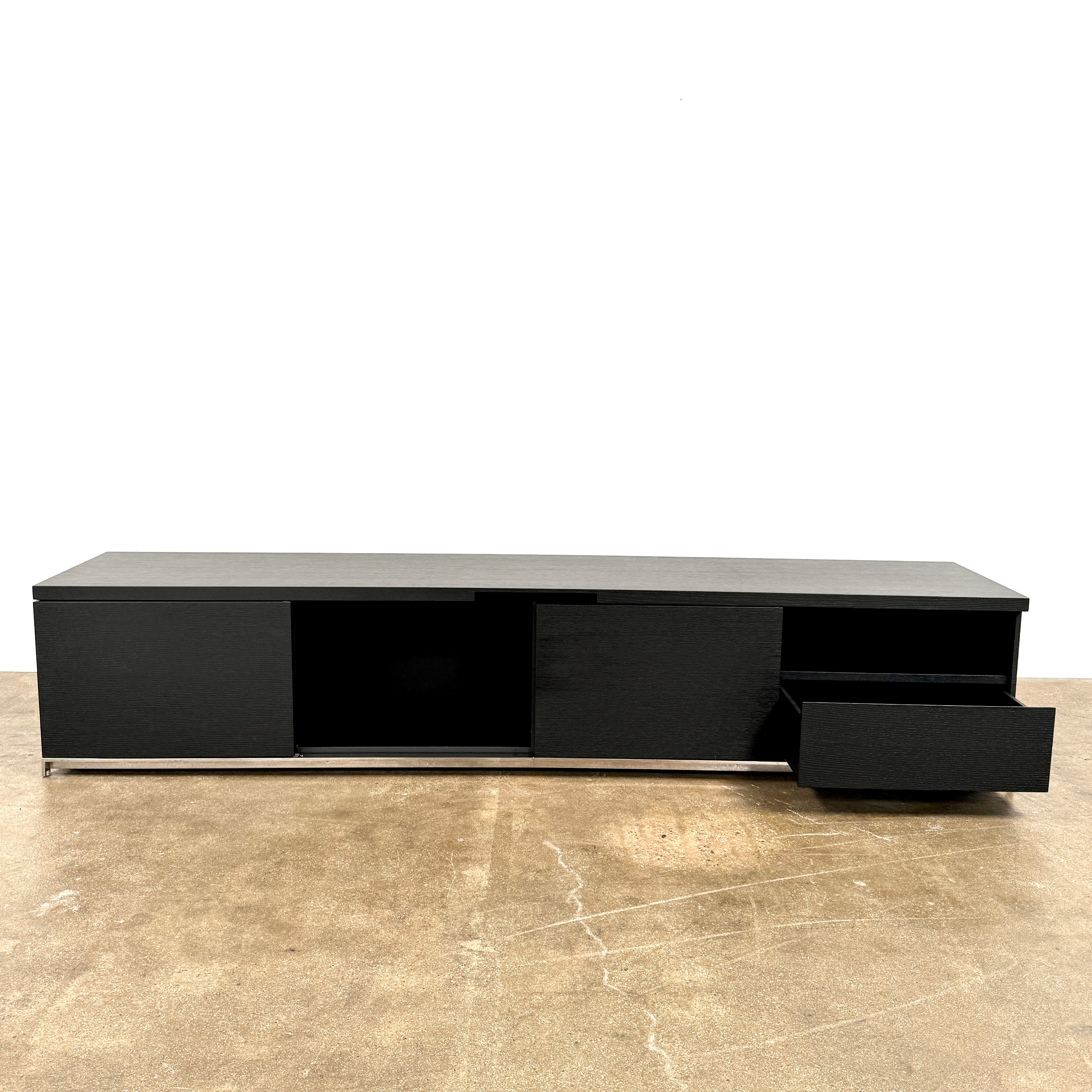The Maxalto Mida Console by Maxalto is a modern black sideboard TV stand with three closed cabinets and two open shelves, shown on a concrete floor against a plain white background.