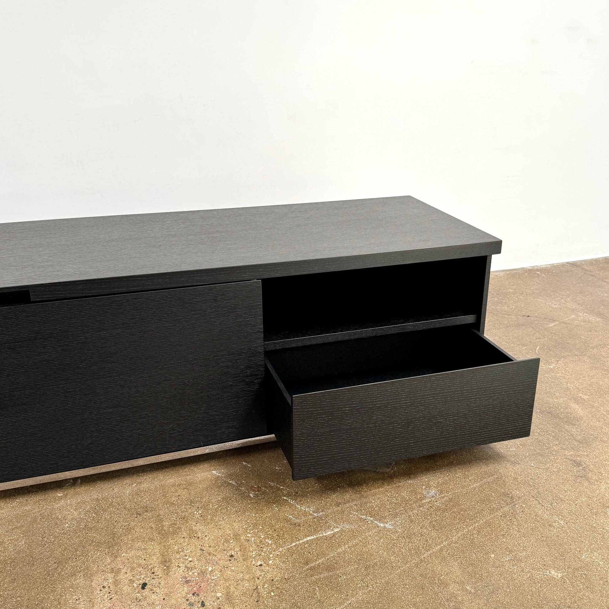 The Maxalto Mida Console by Maxalto is a modern black sideboard TV stand with three closed cabinets and two open shelves, shown on a concrete floor against a plain white background.