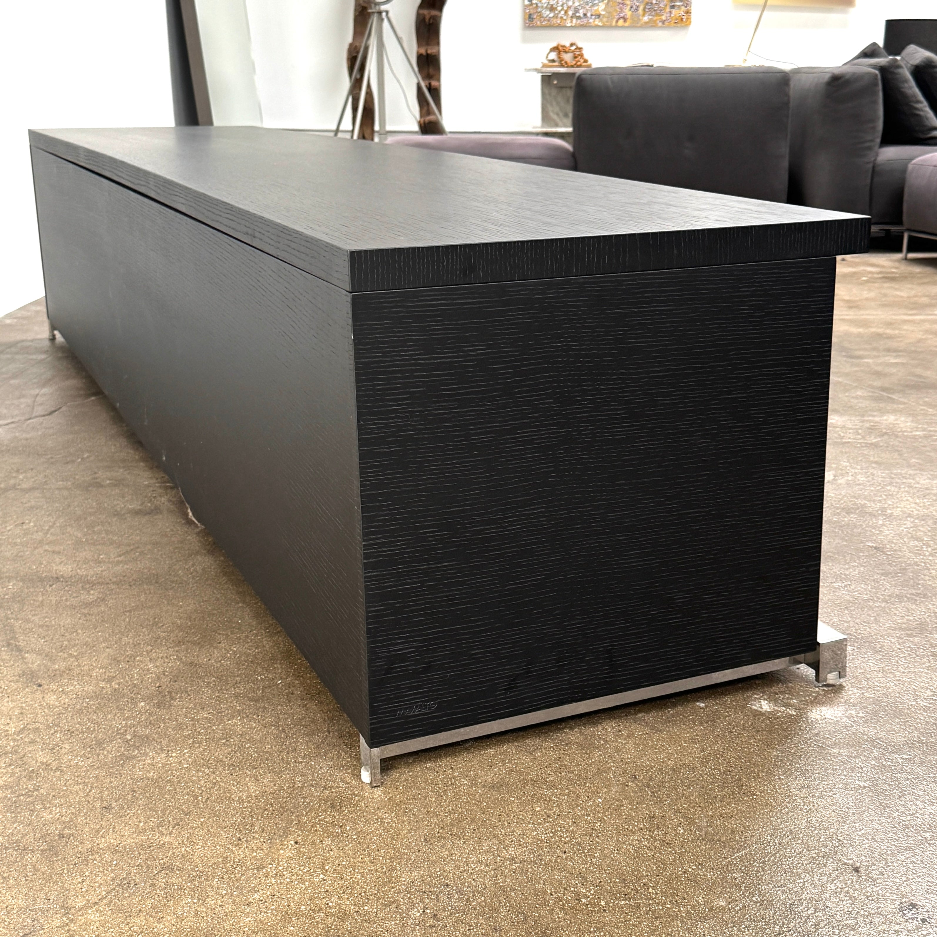 The Maxalto Mida Console by Maxalto is a modern black sideboard TV stand with three closed cabinets and two open shelves, shown on a concrete floor against a plain white background.