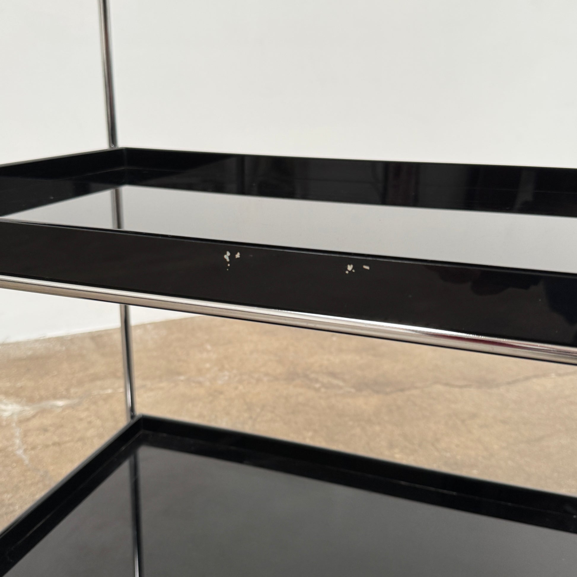 The Kartell Trays Trolly by Kartell features three black metal tiers, glass shelves, and four wheels, displayed on a plain white background.