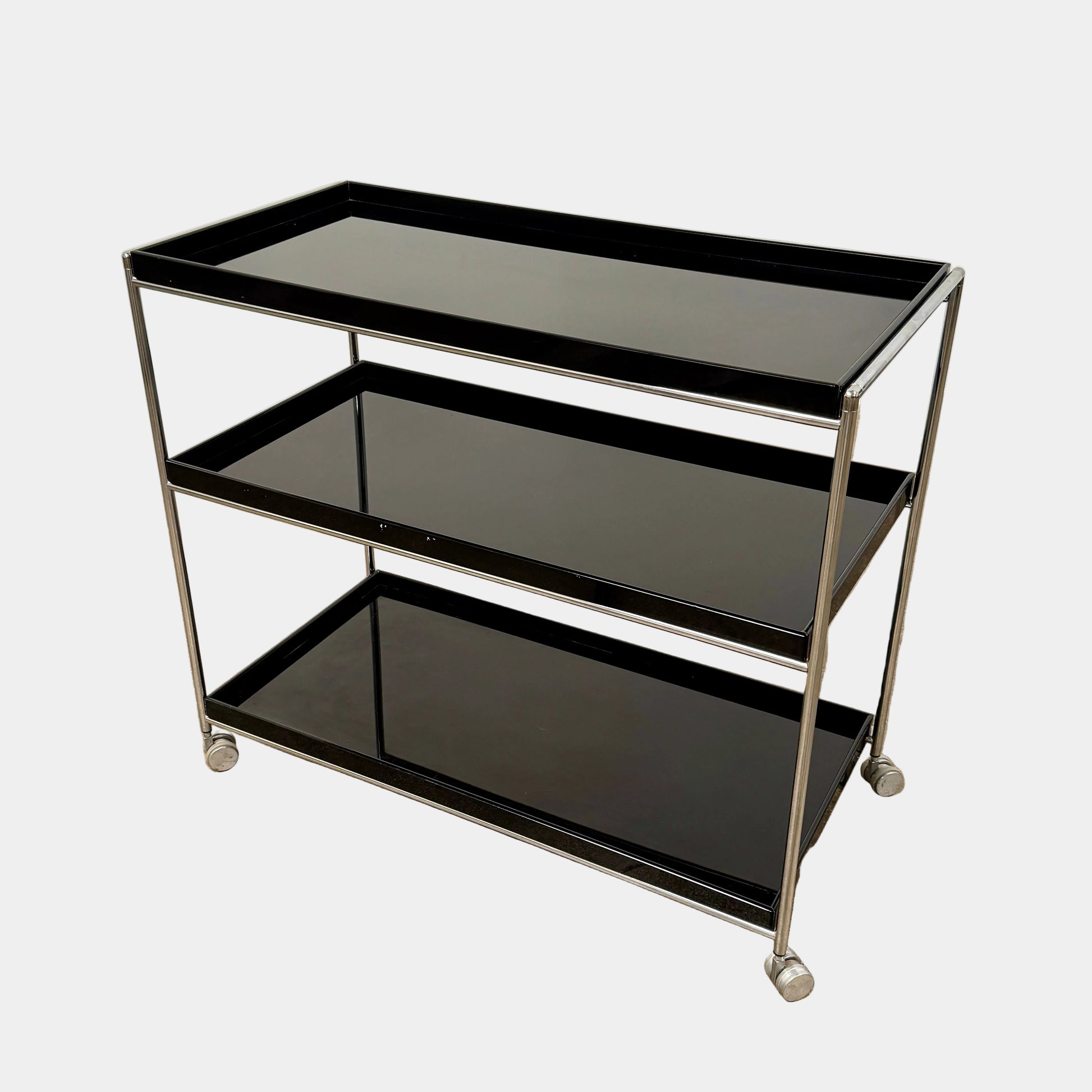 The Kartell Trays Trolly by Kartell features three black metal tiers, glass shelves, and four wheels, displayed on a plain white background.