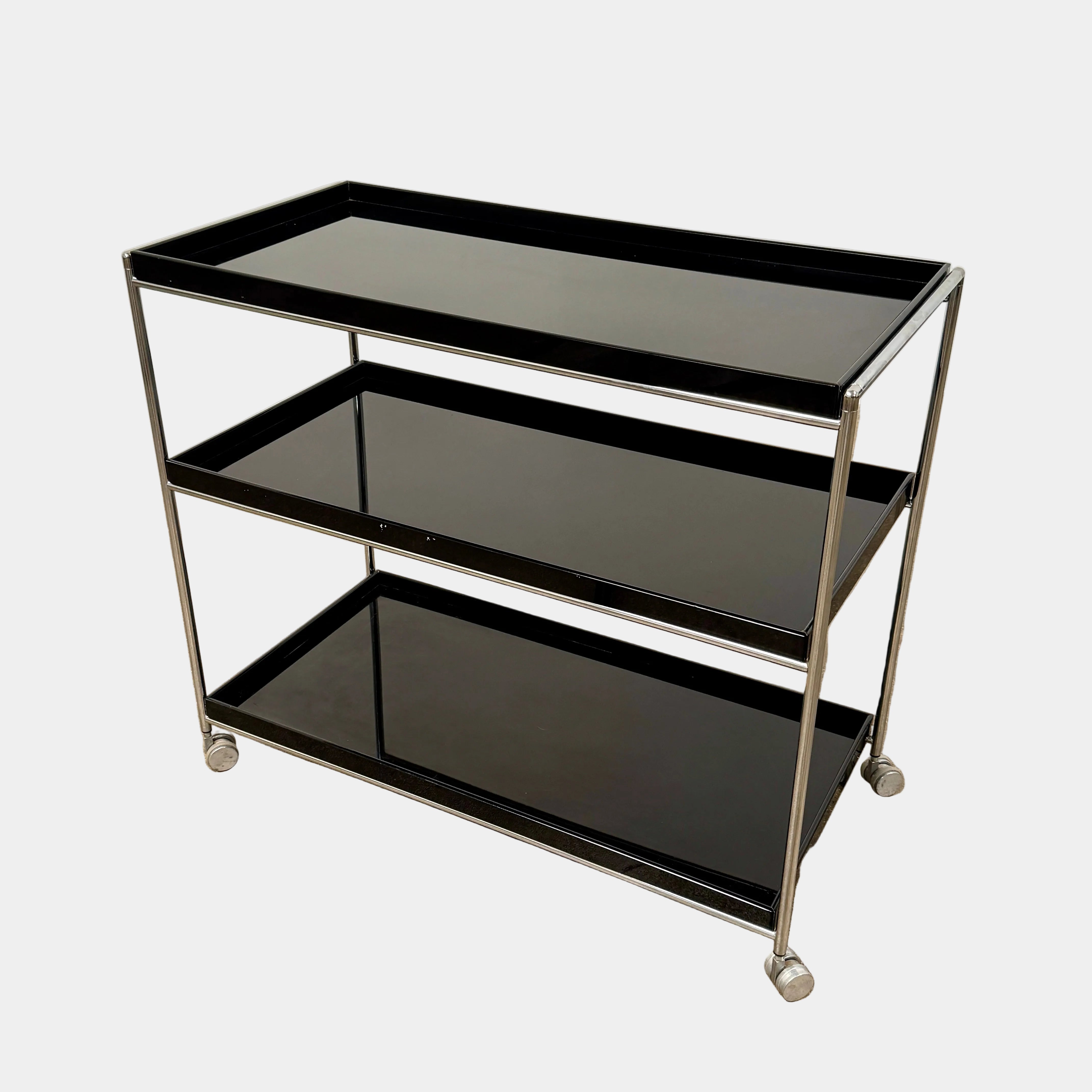 The Kartell Trays Trolly by Kartell features three black metal tiers, glass shelves, and four wheels, displayed on a plain white background.