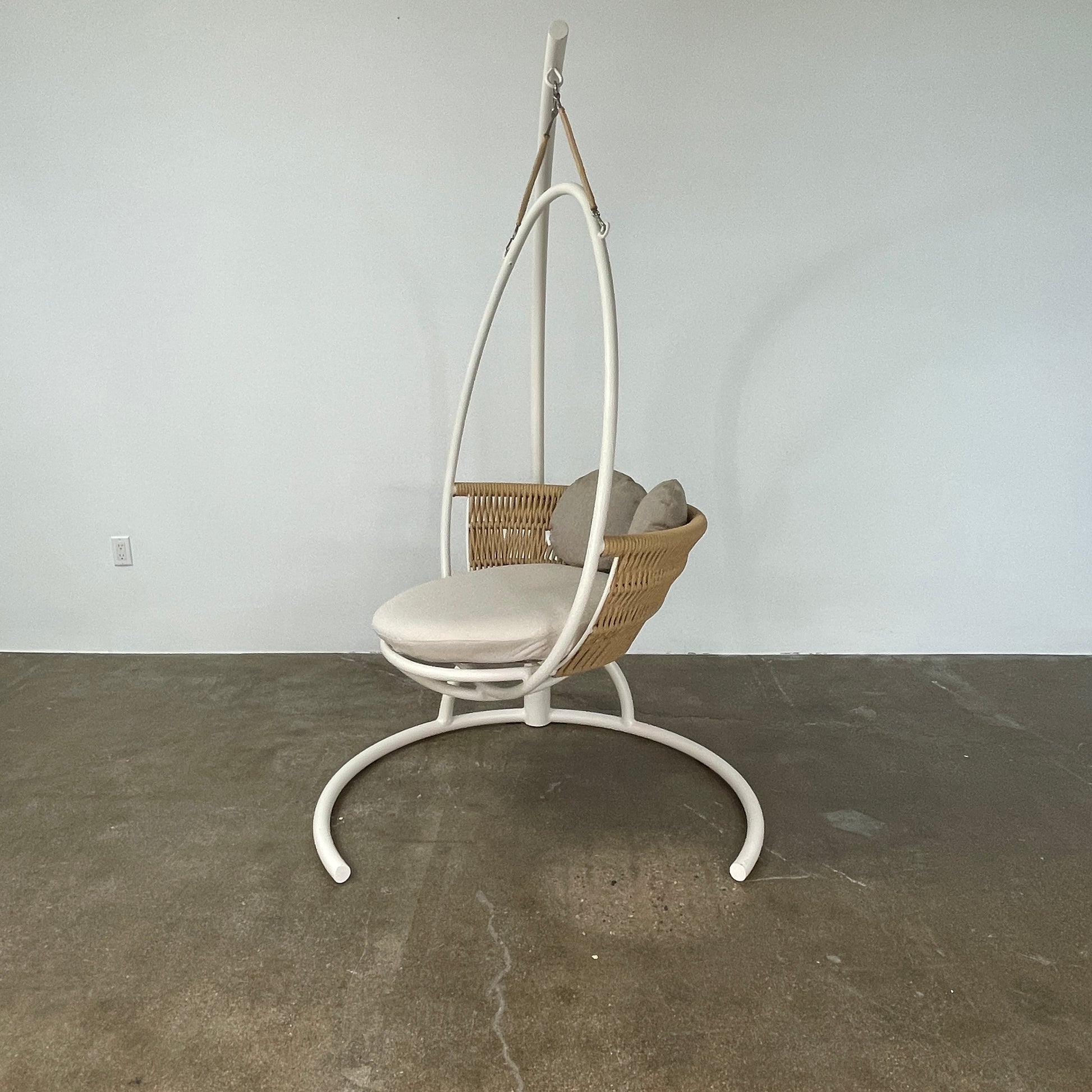 The Point 1920 Weave Hanging Swing with Base by Modern Resale features a white metal frame, wicker seat, and beige cushions, shown freestanding and isolated on a plain white background.