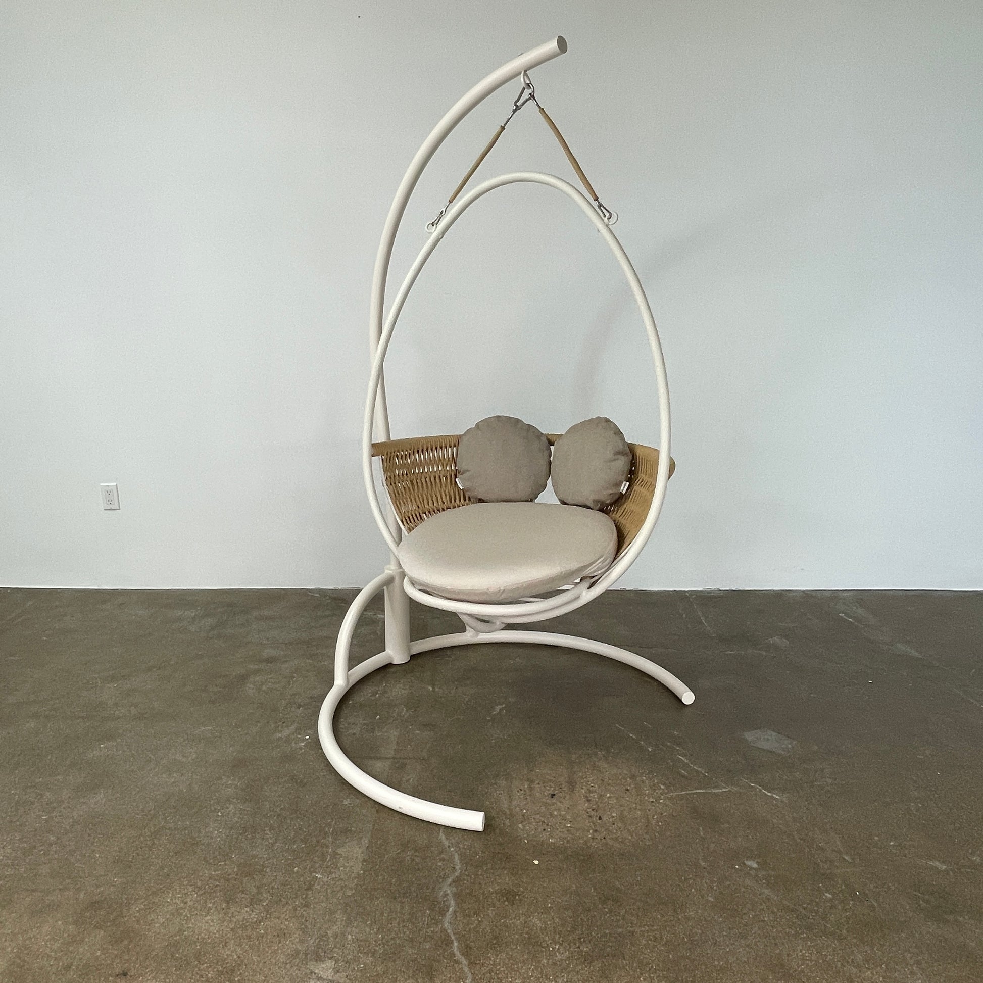 The Point 1920 Weave Hanging Swing with Base by Modern Resale features a white metal frame, wicker seat, and beige cushions, shown freestanding and isolated on a plain white background.