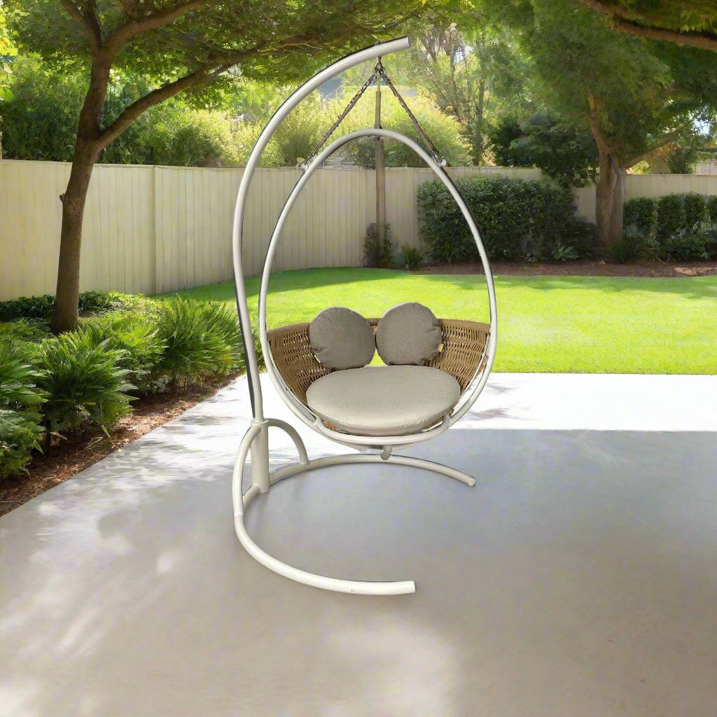 The Point 1920 Weave Hanging Swing with Base by Modern Resale features a white metal frame, wicker seat, and beige cushions, shown freestanding and isolated on a plain white background.