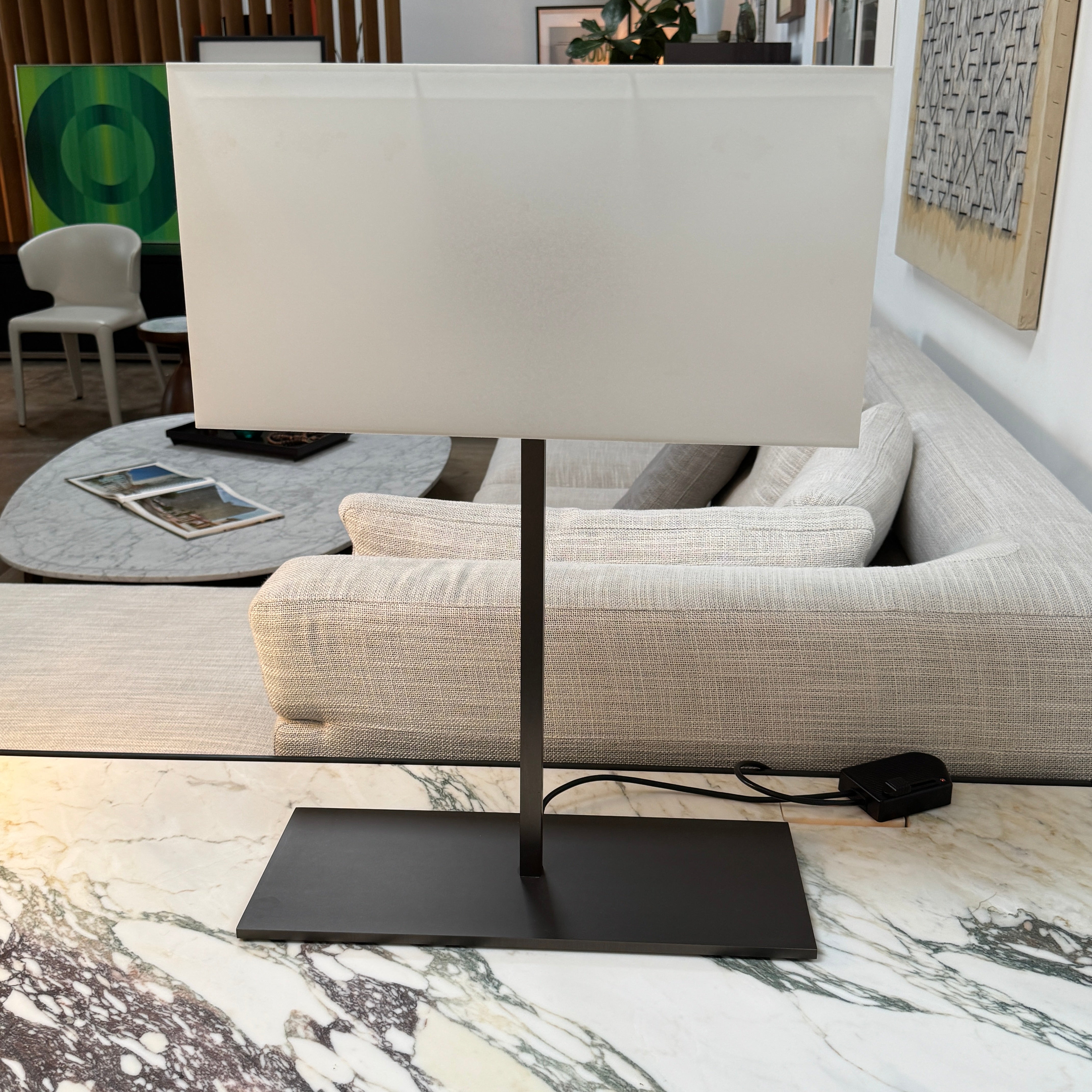 The Maxalto Leukon Table Lamp by Maxalto features a rectangular fabric shade, slim metal stem, and flat base, providing warm, modern lighting.