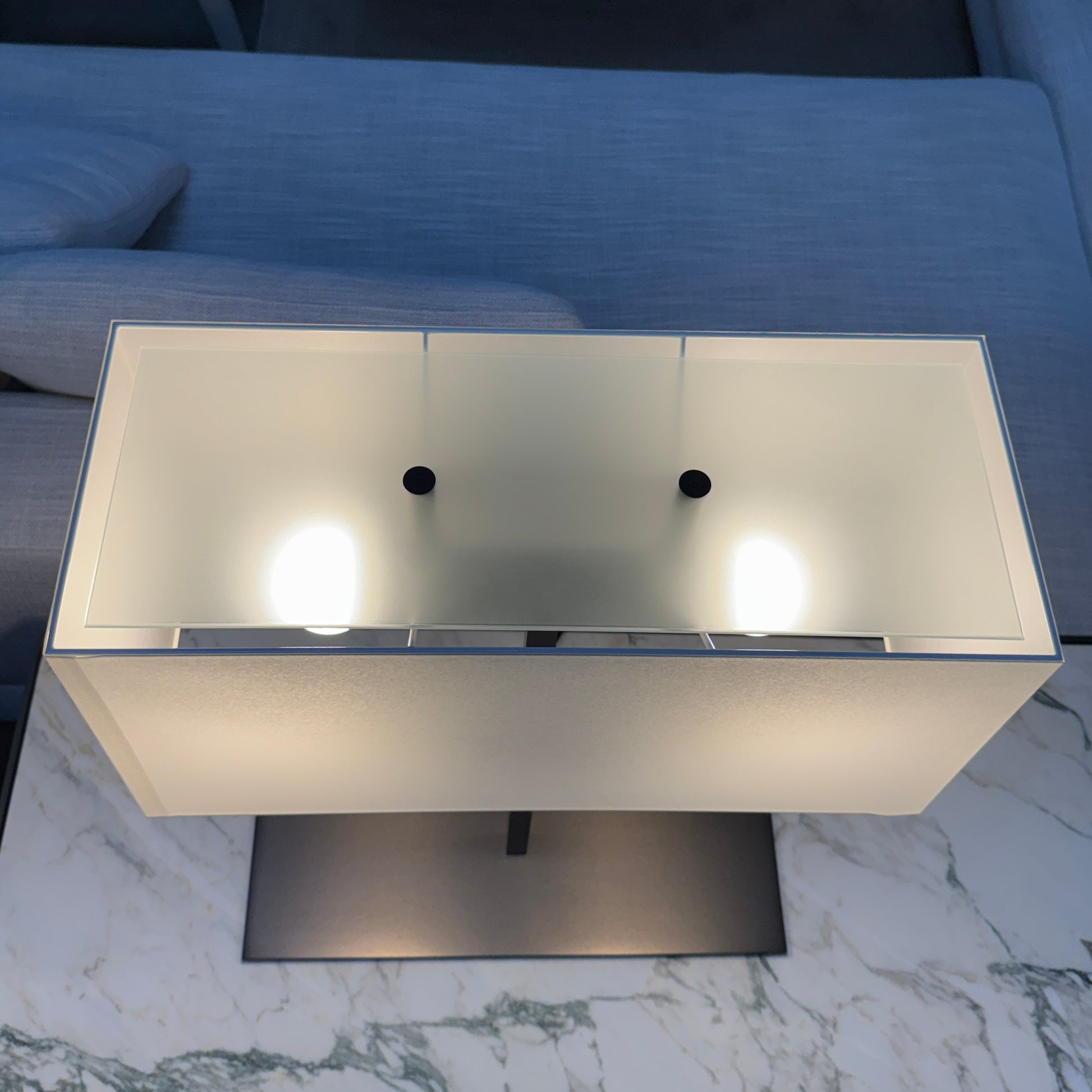 The Maxalto Leukon Table Lamp by Maxalto features a rectangular fabric shade, slim metal stem, and flat base, providing warm, modern lighting.