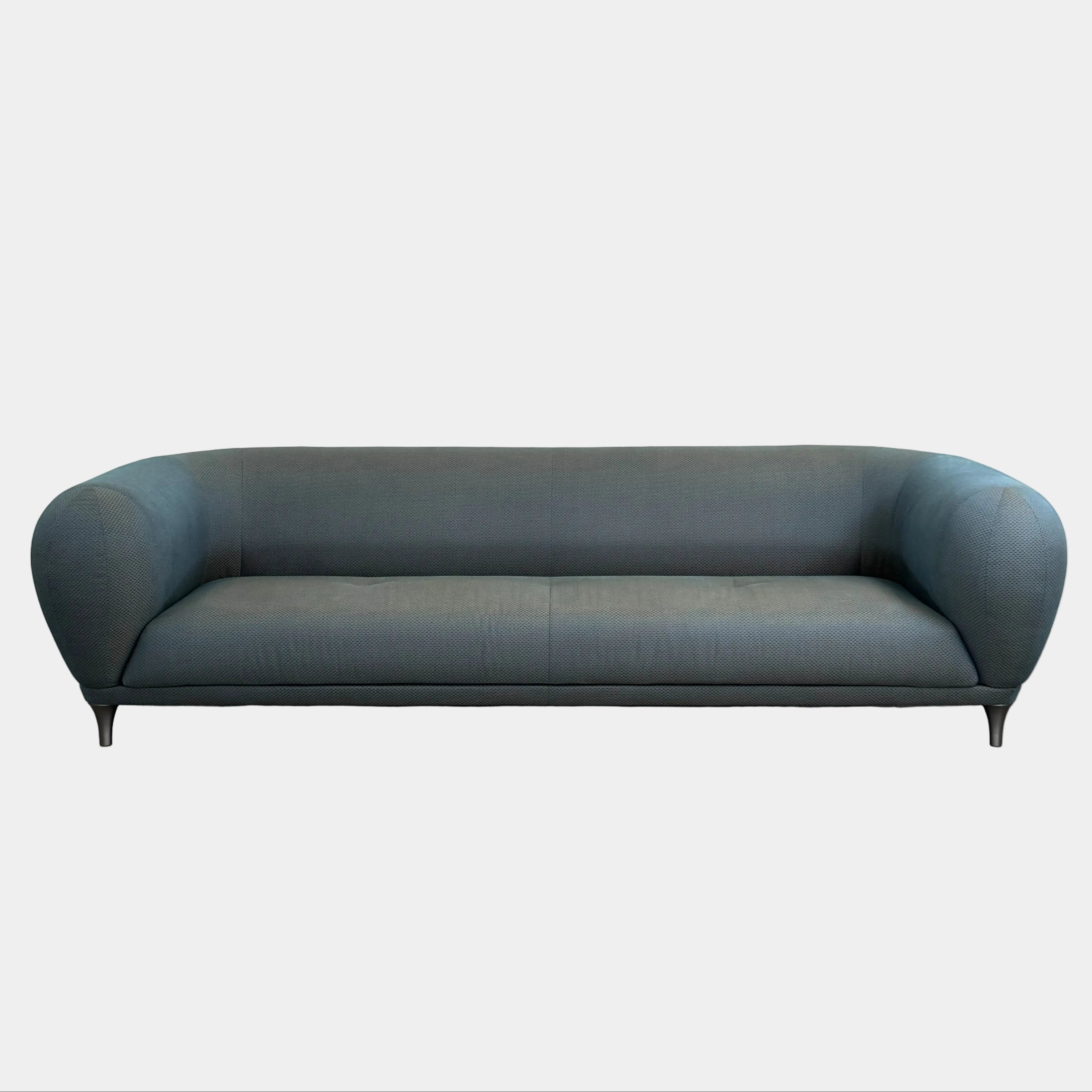 A Roche Bobois Montgolfiere sofa in dark gray, featuring rounded arms and black legs, from the Globe Trotter collection by Marcel Wanders, sits on a polished concrete floor against a plain white wall.