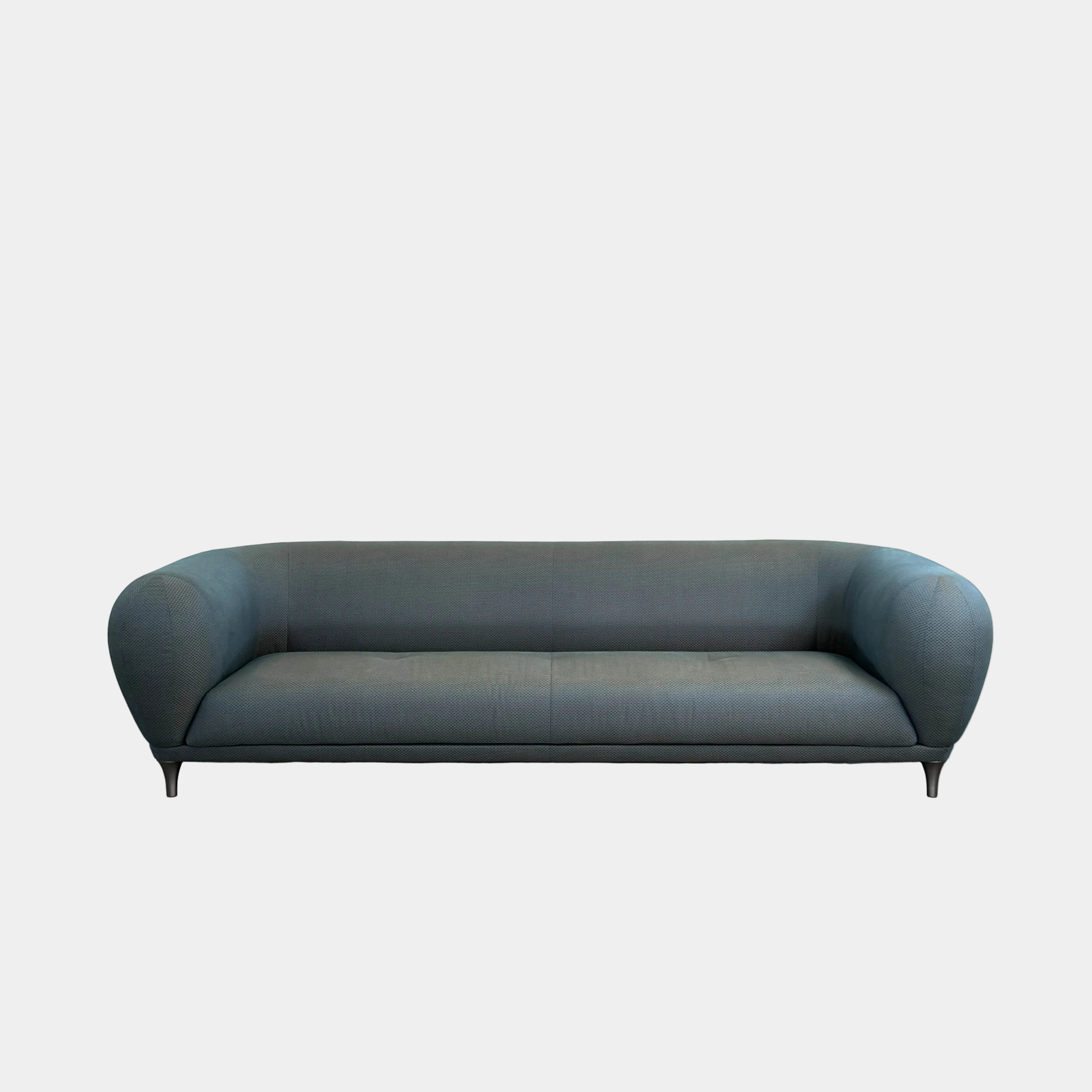 A Roche Bobois Montgolfiere sofa in dark gray, featuring rounded arms and black legs, from the Globe Trotter collection by Marcel Wanders, sits on a polished concrete floor against a plain white wall.