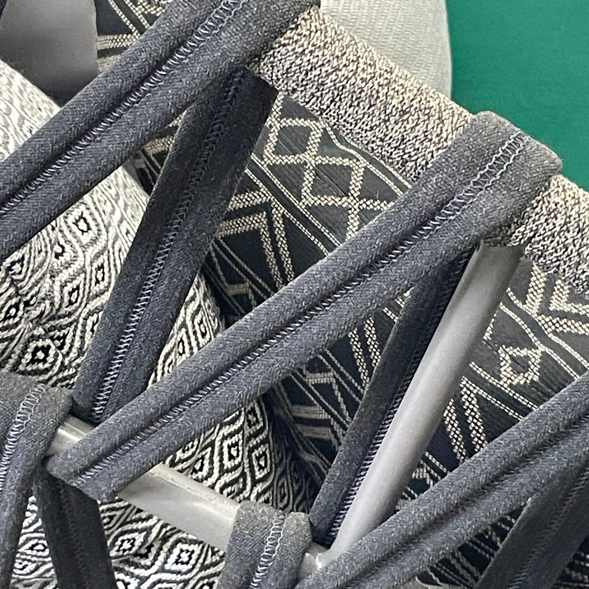 A Varaschin Outdoor Emma Cross Daybed in black with a green cushion and five assorted gray and black pillows rests on a concrete floor by a plain white wall.