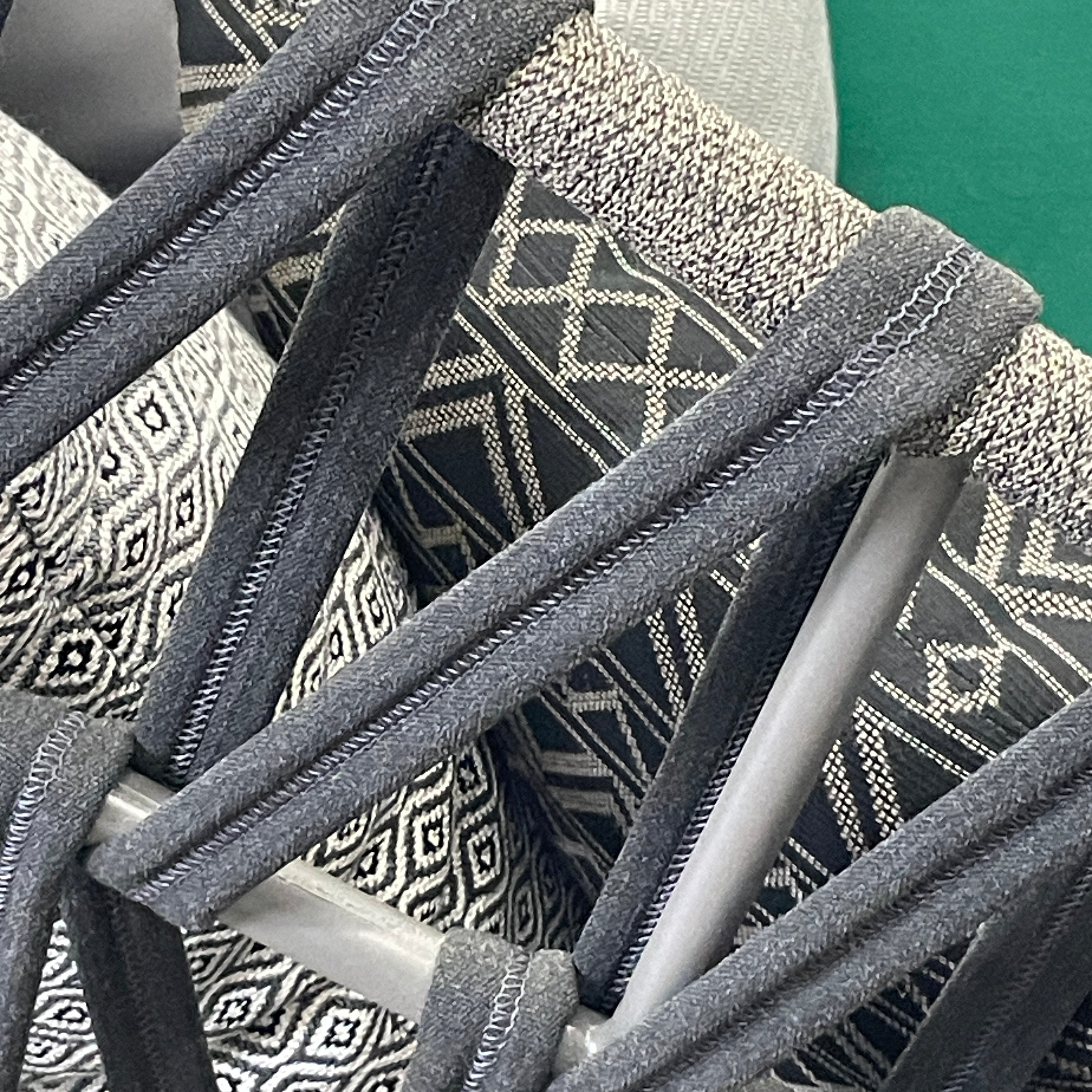 A Varaschin Outdoor Emma Cross Daybed in black with a green cushion and five assorted gray and black pillows rests on a concrete floor by a plain white wall.