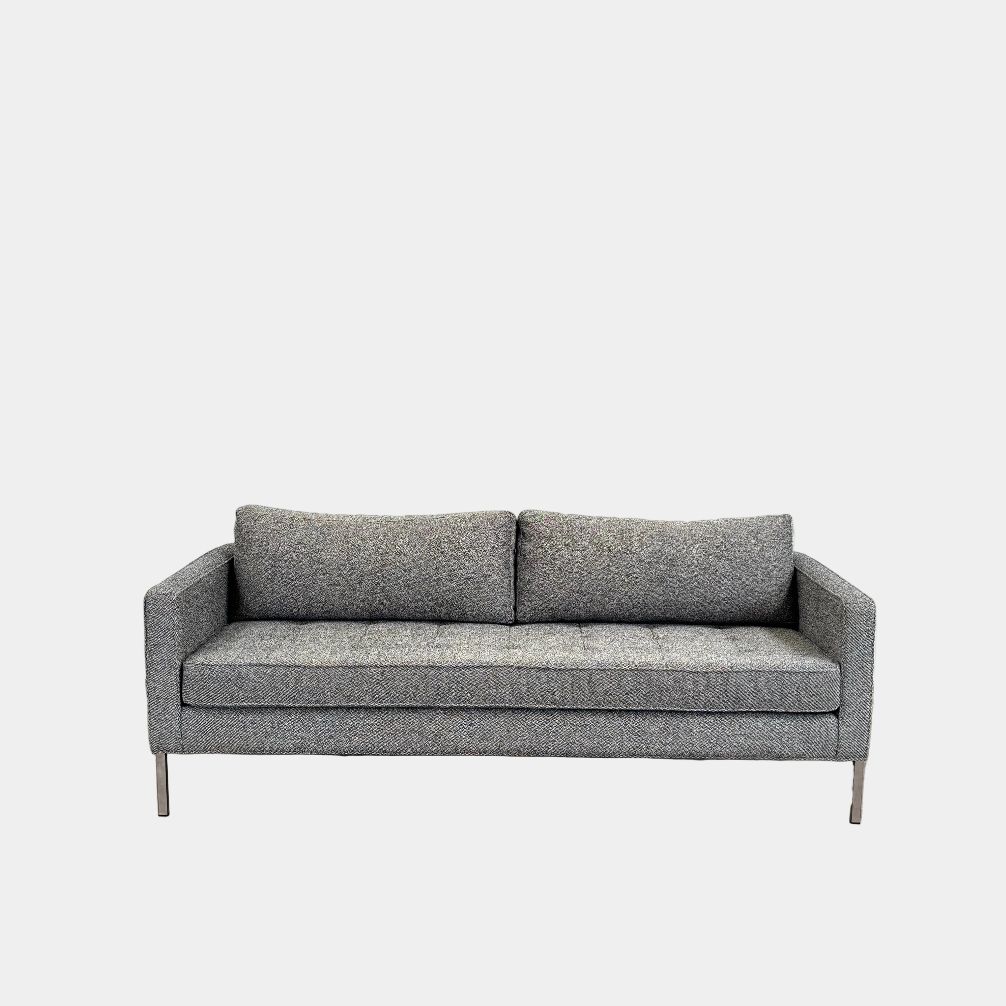The Blu Dot Paramont Sofa is a grey, three-seater sofa by Blu Dot, featuring metal legs and two back cushions, shown against a plain white background.