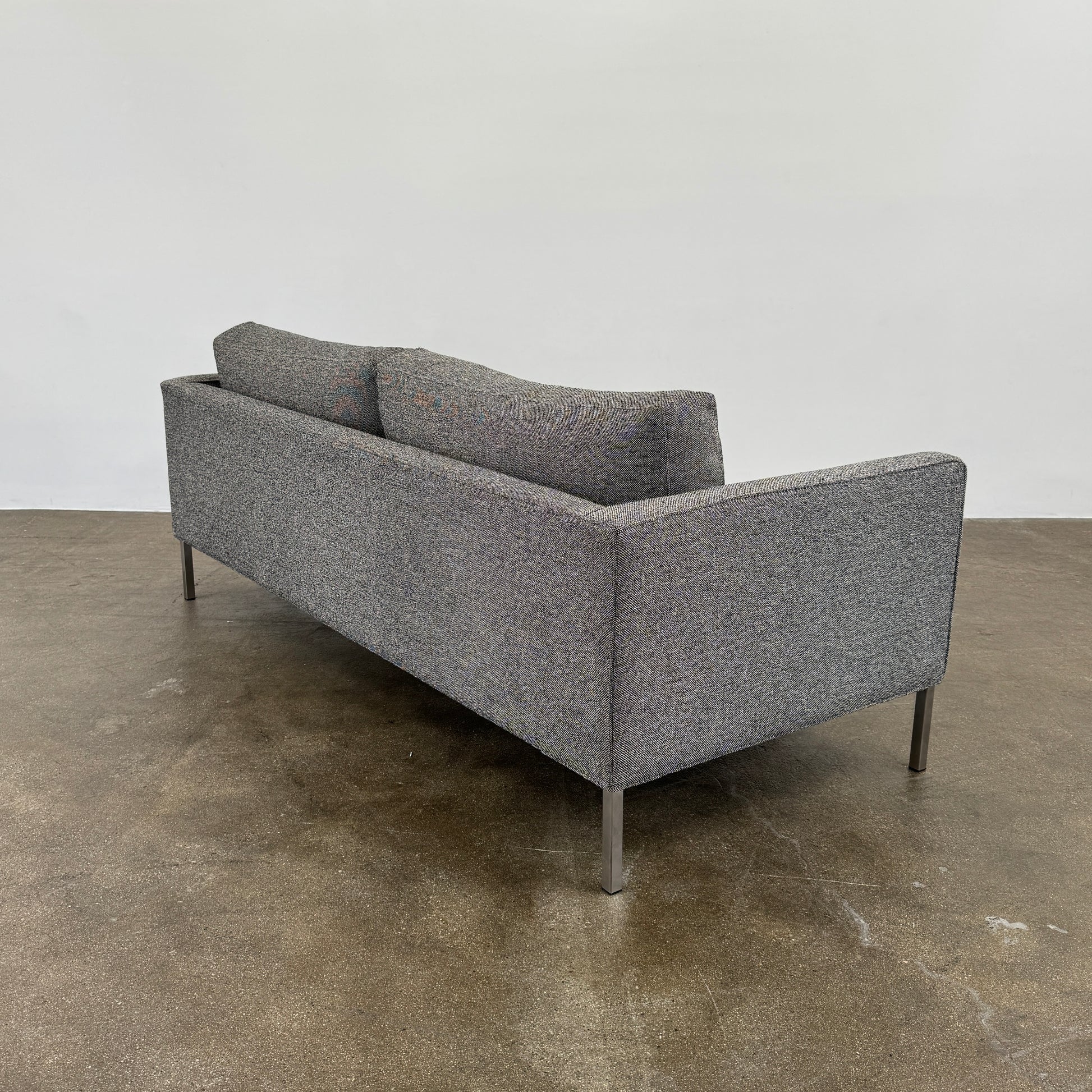 The Blu Dot Paramont Sofa is a grey, three-seater sofa by Blu Dot, featuring metal legs and two back cushions, shown against a plain white background.