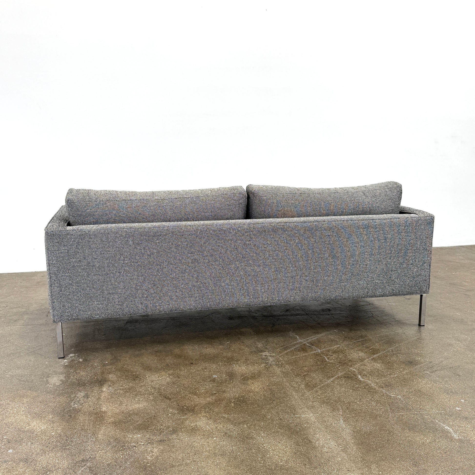 The Blu Dot Paramont Sofa is a grey, three-seater sofa by Blu Dot, featuring metal legs and two back cushions, shown against a plain white background.
