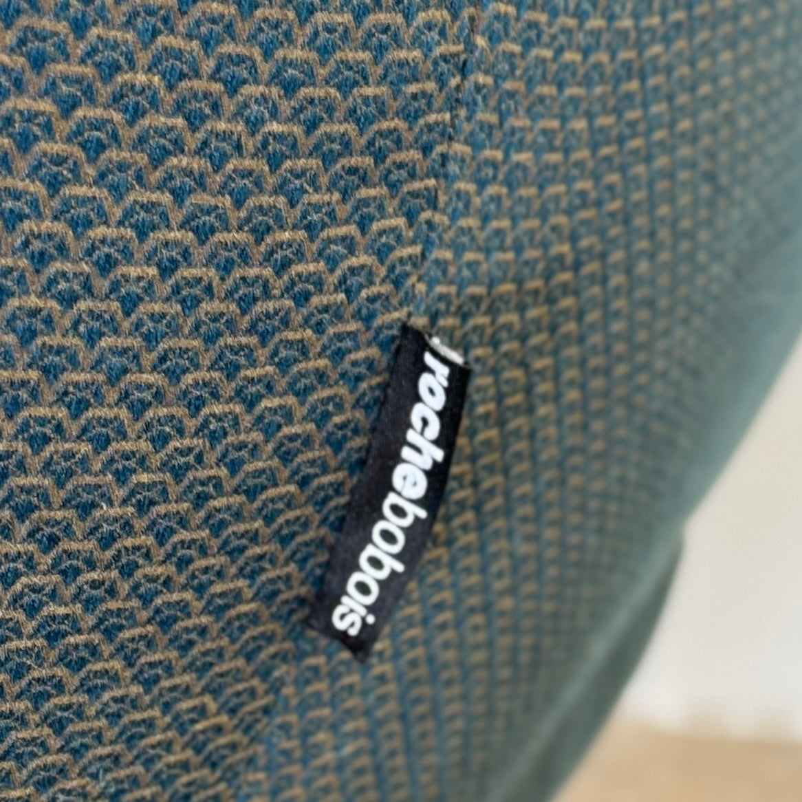 A Roche Bobois Montgolfiere sofa in dark gray, featuring rounded arms and black legs, from the Globe Trotter collection by Marcel Wanders, sits on a polished concrete floor against a plain white wall.