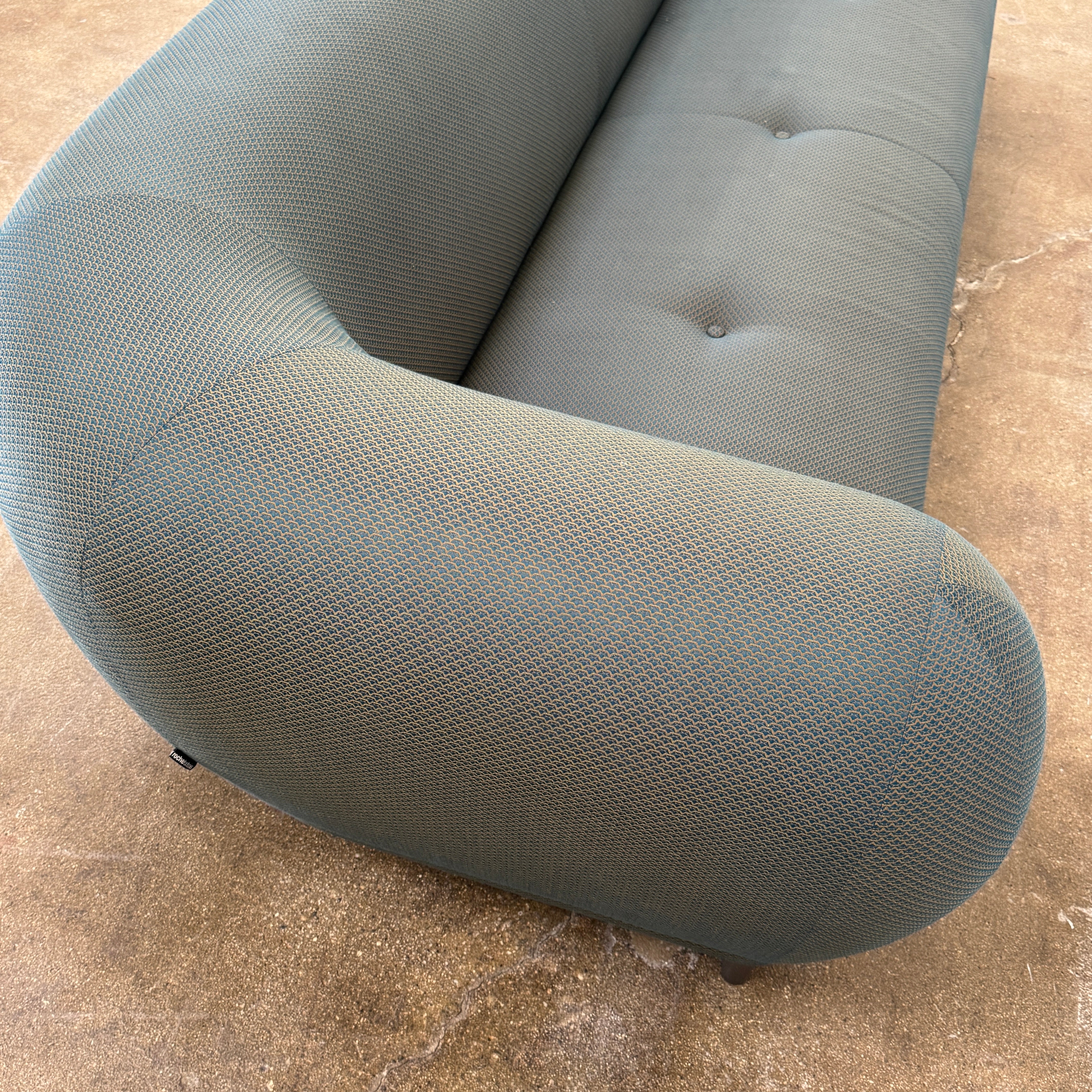 A Roche Bobois Montgolfiere sofa in dark gray, featuring rounded arms and black legs, from the Globe Trotter collection by Marcel Wanders, sits on a polished concrete floor against a plain white wall.