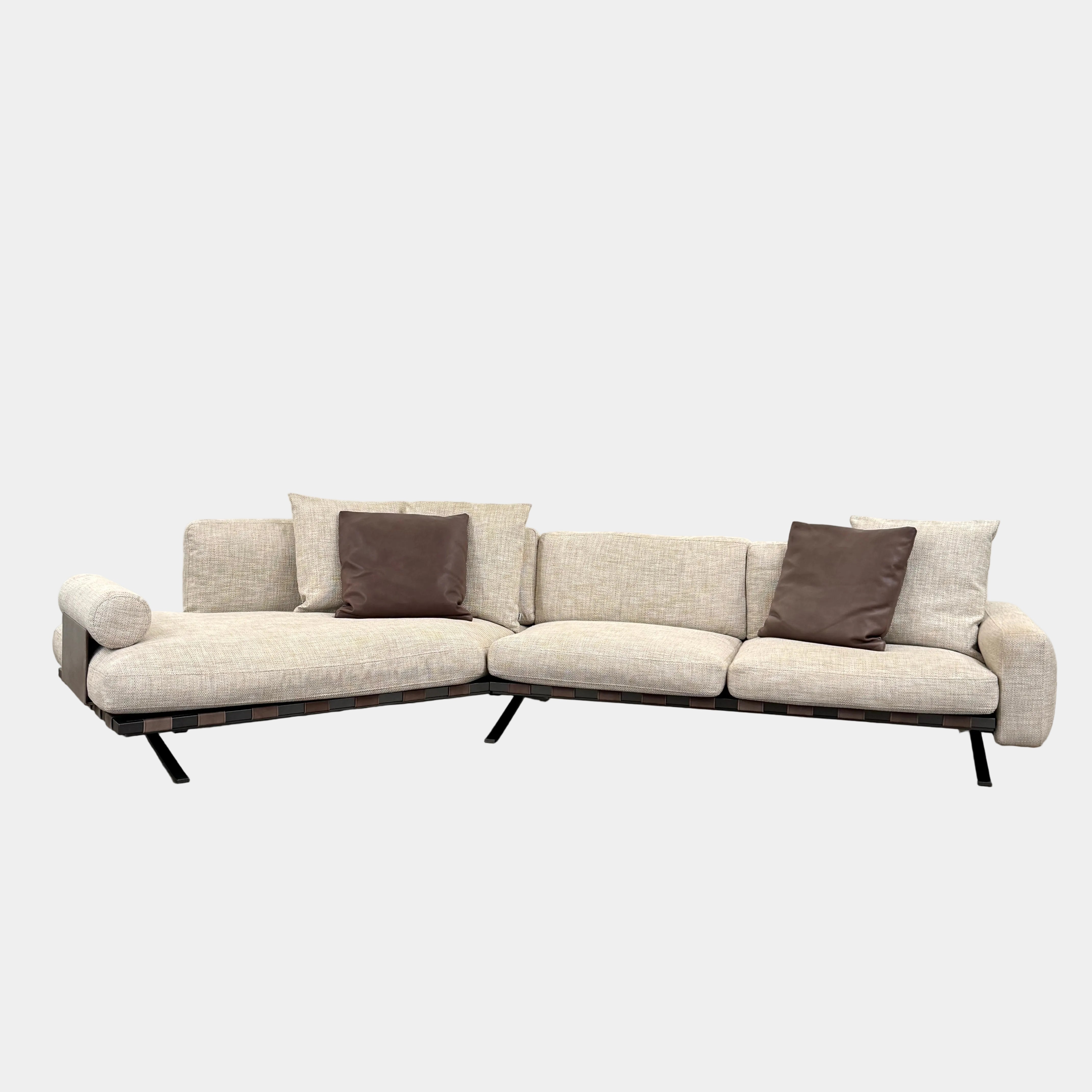 The Driade Fenix sofa by Driade is a beige L-shaped modular design with three seat cushions, black legs, and four throw pillows—two brown, two beige—highlighting its architectural lightness against a plain white backdrop.