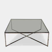 The Smoked Glass Coffee Table features a square design with a contemporary metal frame and crossed support bars, shown against a plain white background. Brand: Unknown.