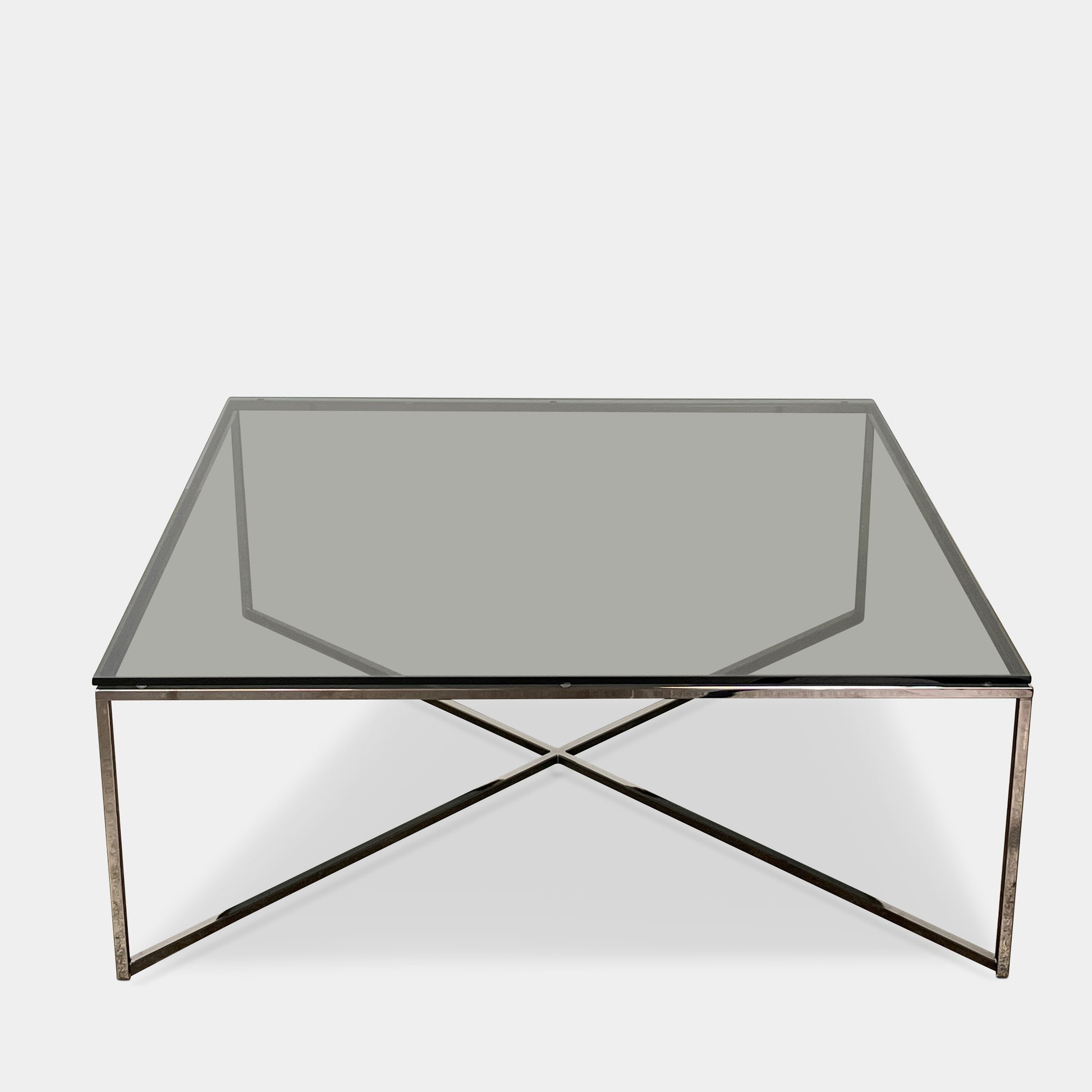 The Smoked Glass Coffee Table features a square design with a contemporary metal frame and crossed support bars, shown against a plain white background. Brand: Unknown.