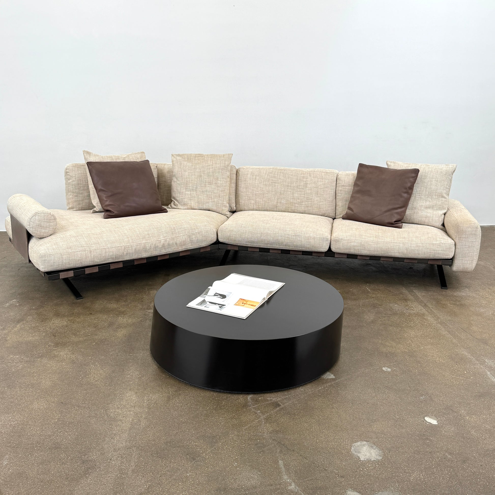The Driade Fenix sofa by Driade is a beige L-shaped modular design with three seat cushions, black legs, and four throw pillows—two brown, two beige—highlighting its architectural lightness against a plain white backdrop.