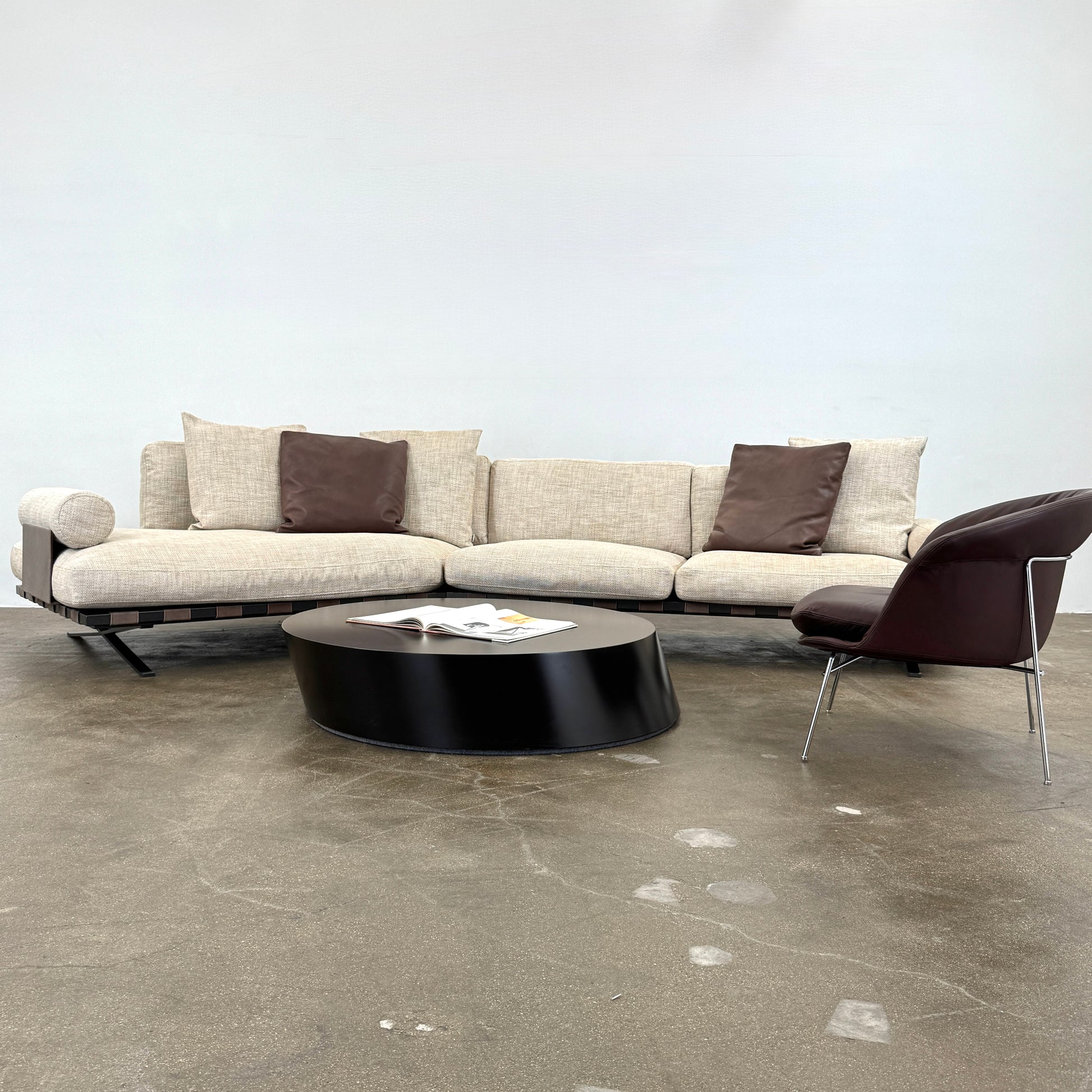 The Driade Fenix sofa by Driade is a beige L-shaped modular design with three seat cushions, black legs, and four throw pillows—two brown, two beige—highlighting its architectural lightness against a plain white backdrop.