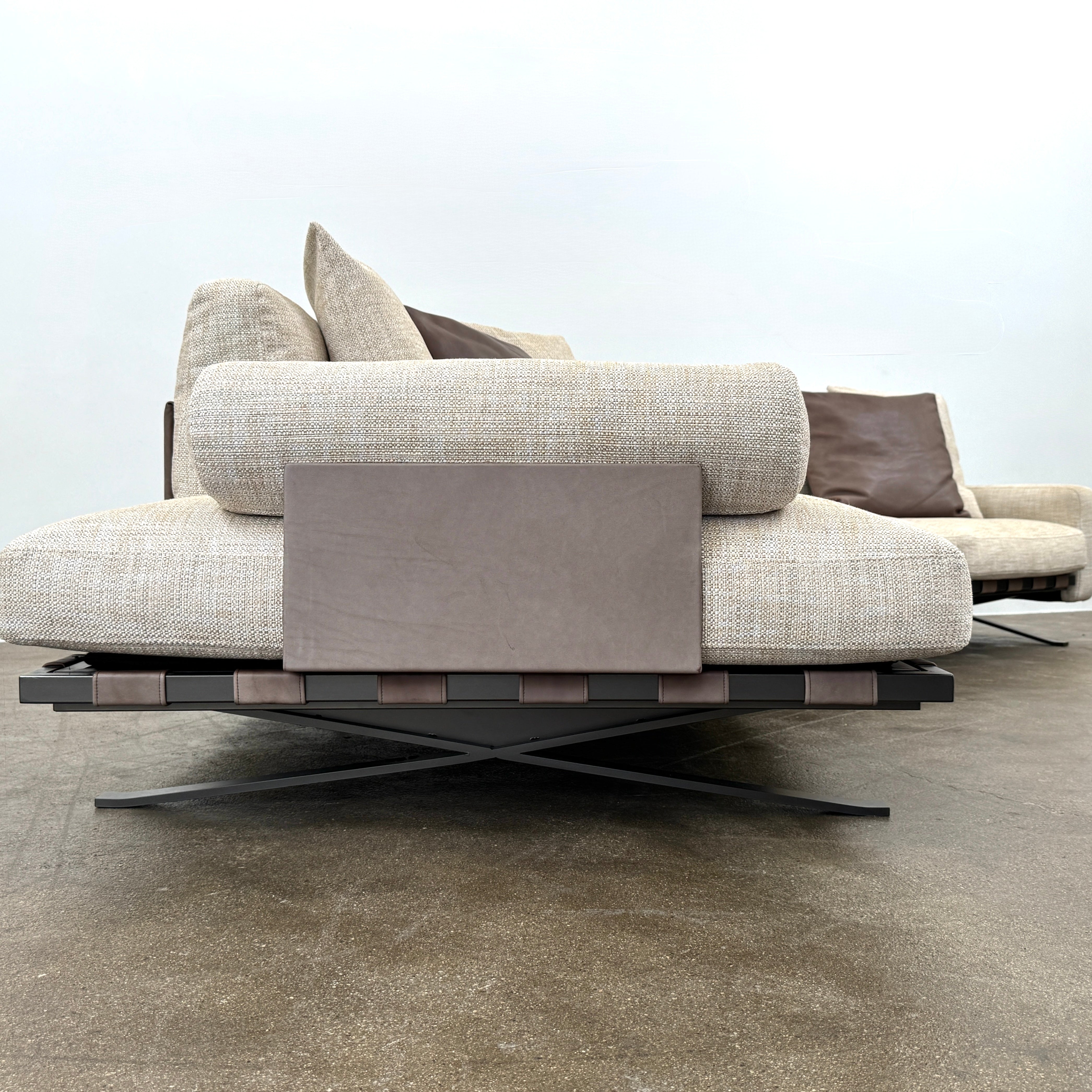 The Driade Fenix sofa by Driade is a beige L-shaped modular design with three seat cushions, black legs, and four throw pillows—two brown, two beige—highlighting its architectural lightness against a plain white backdrop.