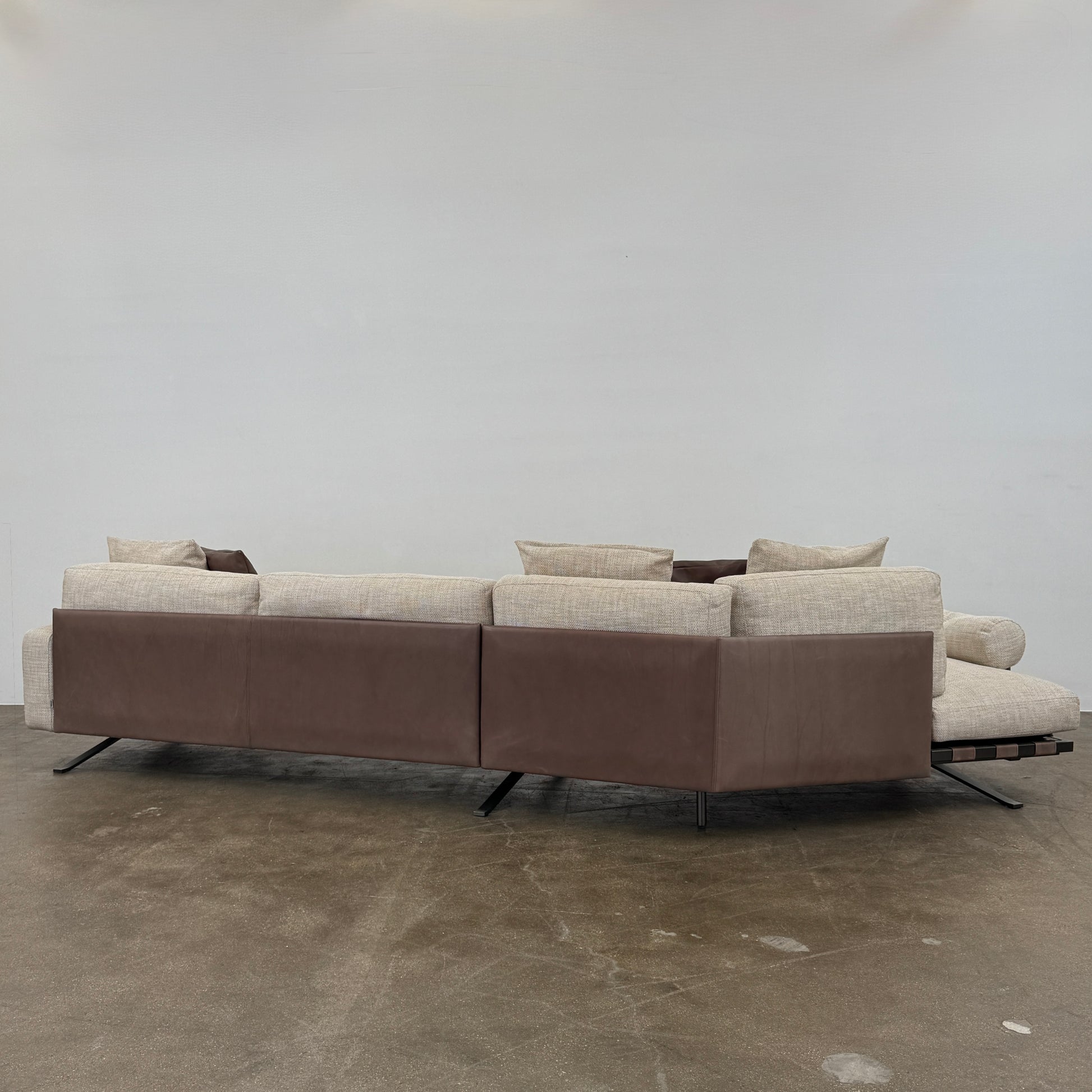 The Driade Fenix sofa by Driade is a beige L-shaped modular design with three seat cushions, black legs, and four throw pillows—two brown, two beige—highlighting its architectural lightness against a plain white backdrop.