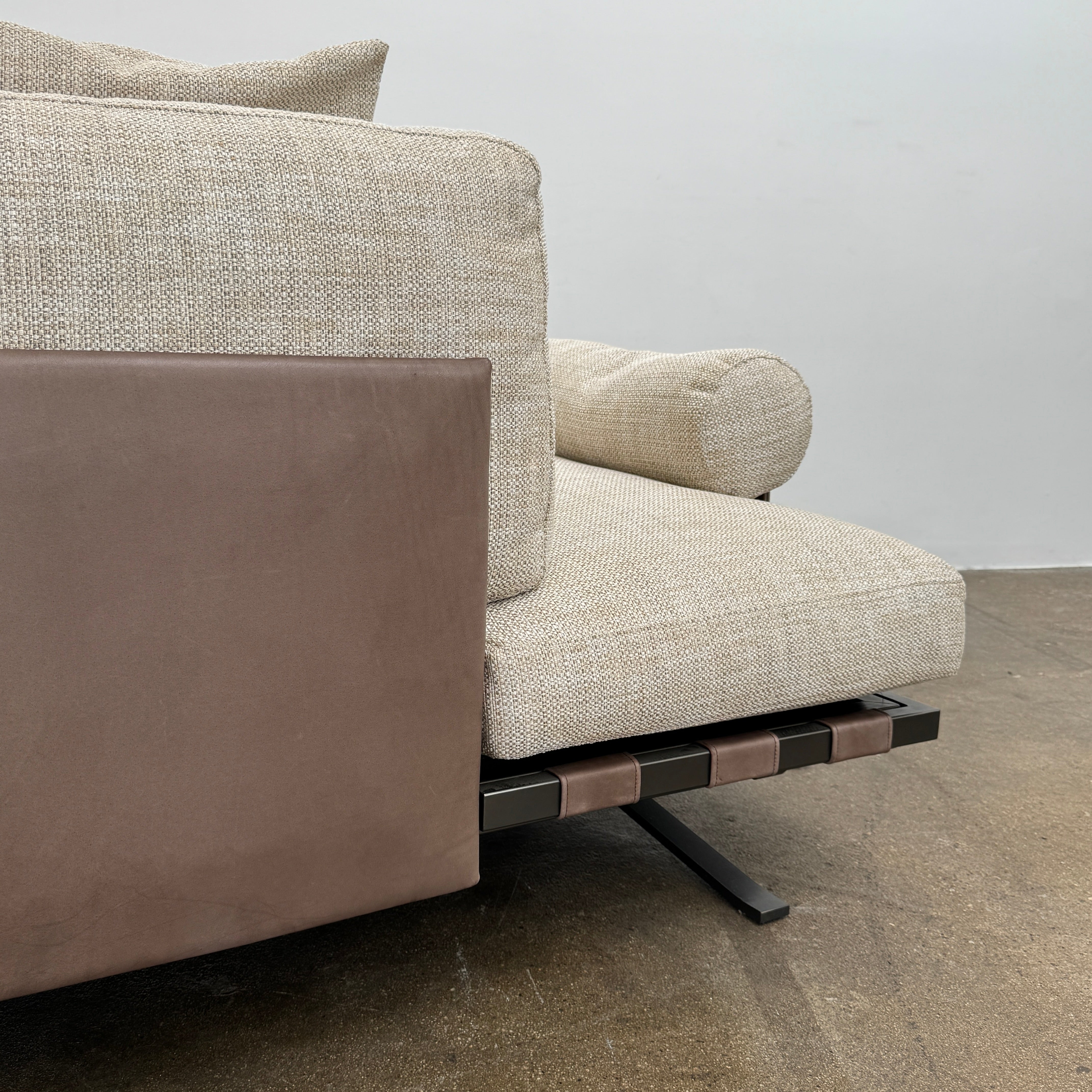 The Driade Fenix sofa by Driade is a beige L-shaped modular design with three seat cushions, black legs, and four throw pillows—two brown, two beige—highlighting its architectural lightness against a plain white backdrop.