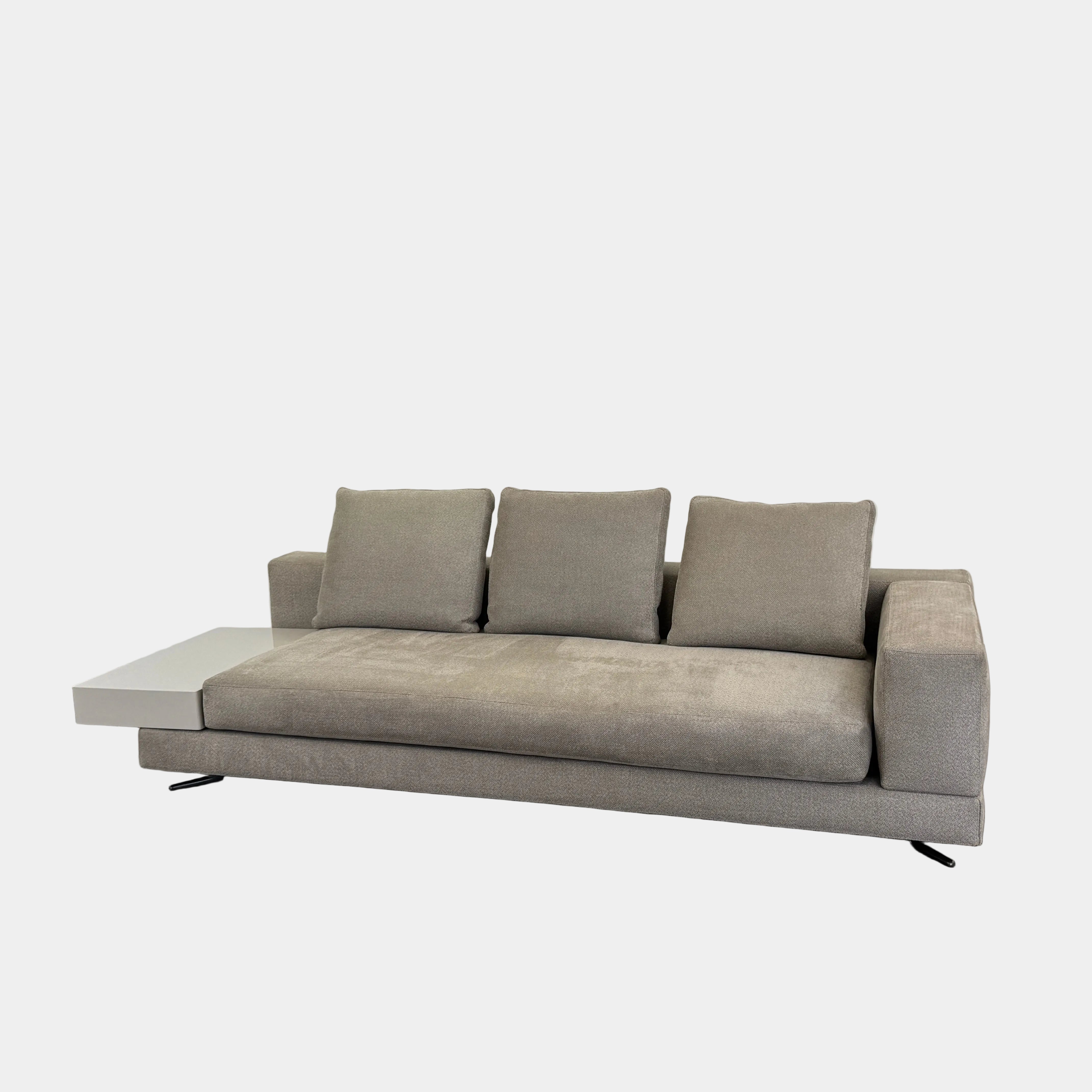 The Minotti White Sofa with Table is a beige three-seater luxury sofa featuring chenille upholstery, wide armrests, three back cushions, and an attached white side table on the right, set against a plain white wall on a brown floor.