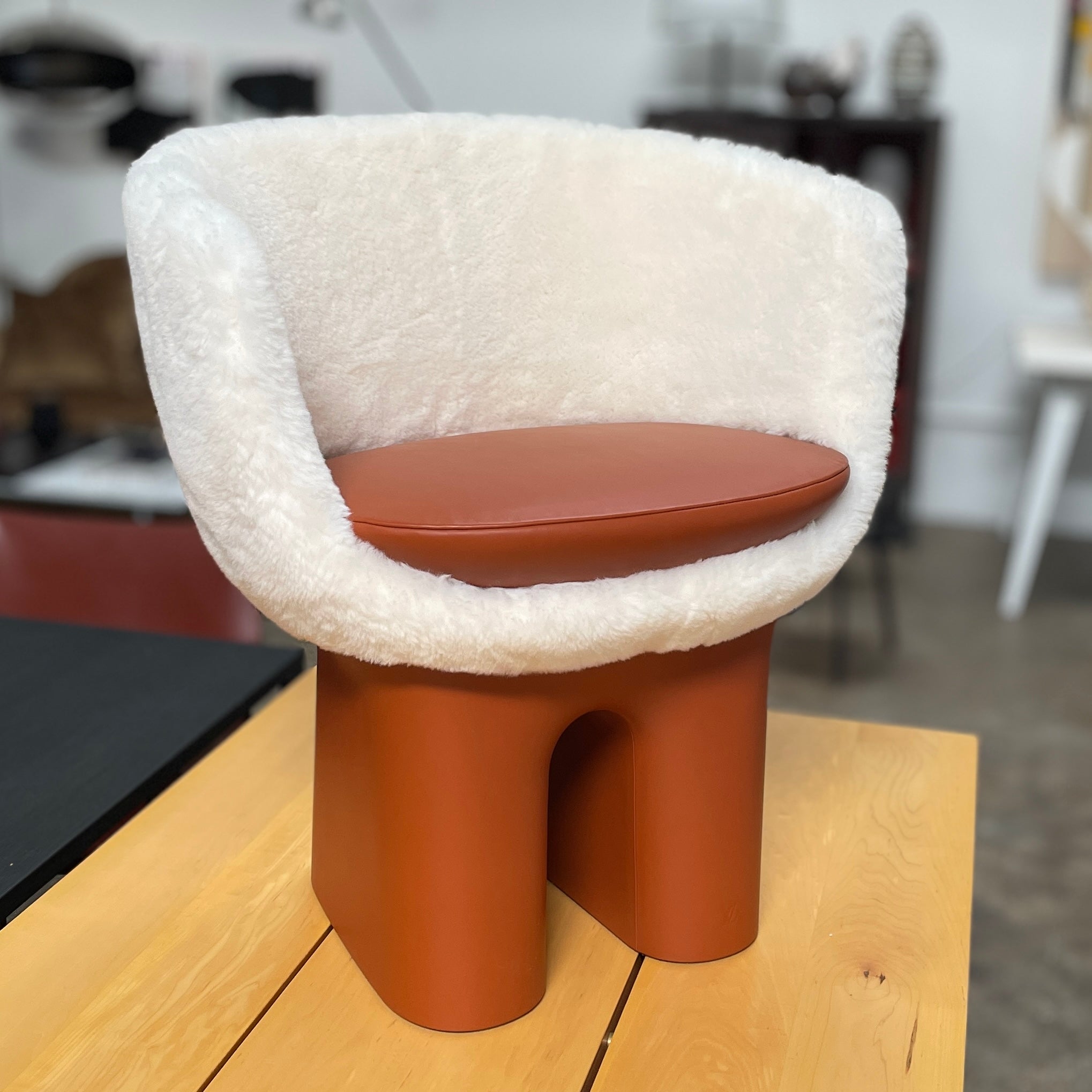 The Louis Vuitton Dolls Fur by Raw Edges is a modern chair with a curved white fluffy leather and fur seat, two short cylindrical brown legs, and a matching brown base, designed by Louis Vuitton and set against a plain background.