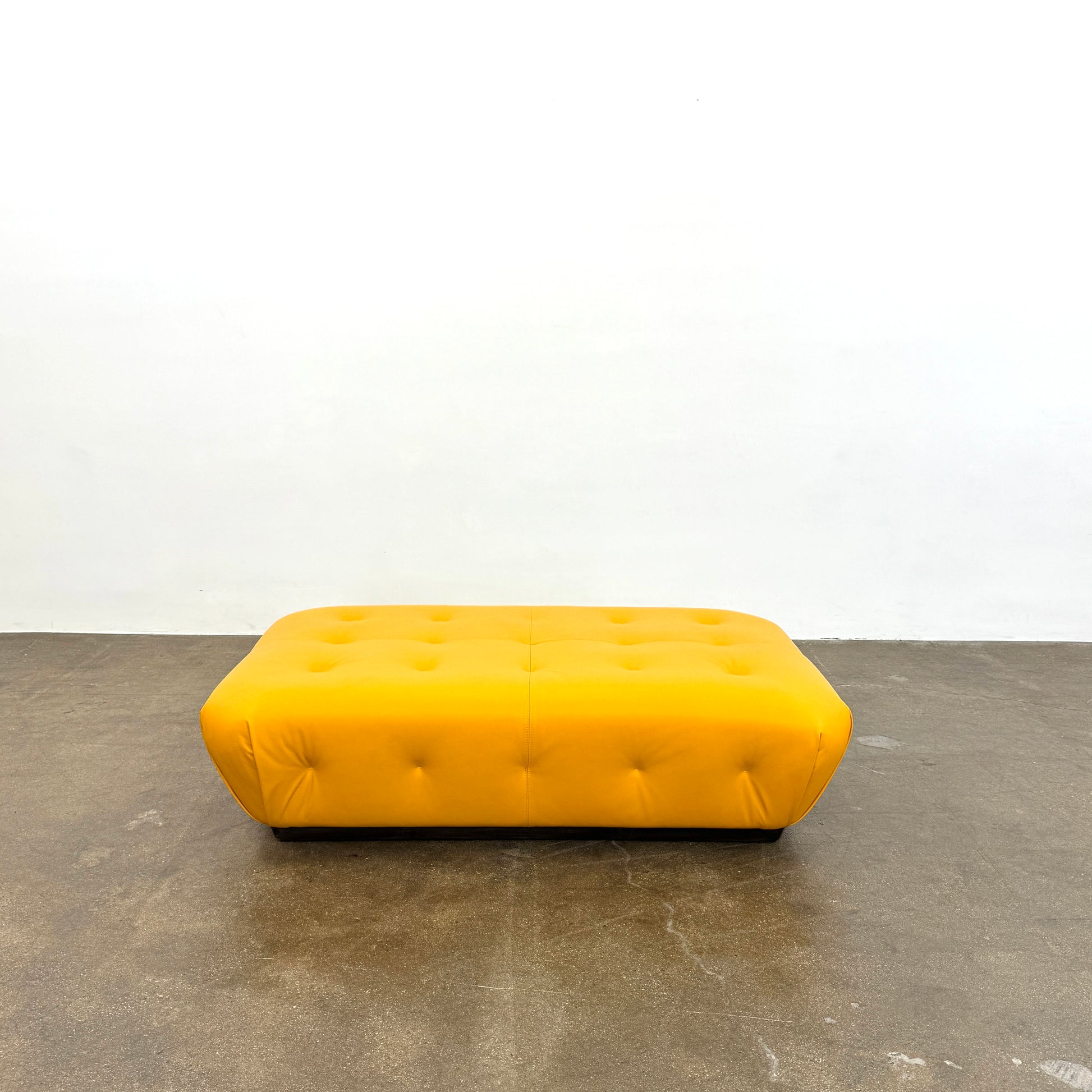 Yellow rectangular Tufted Leather Ottoman with rounded edges and a flat black base, ideal for extra seating, displayed on a plain white background. Brand: Unknown.