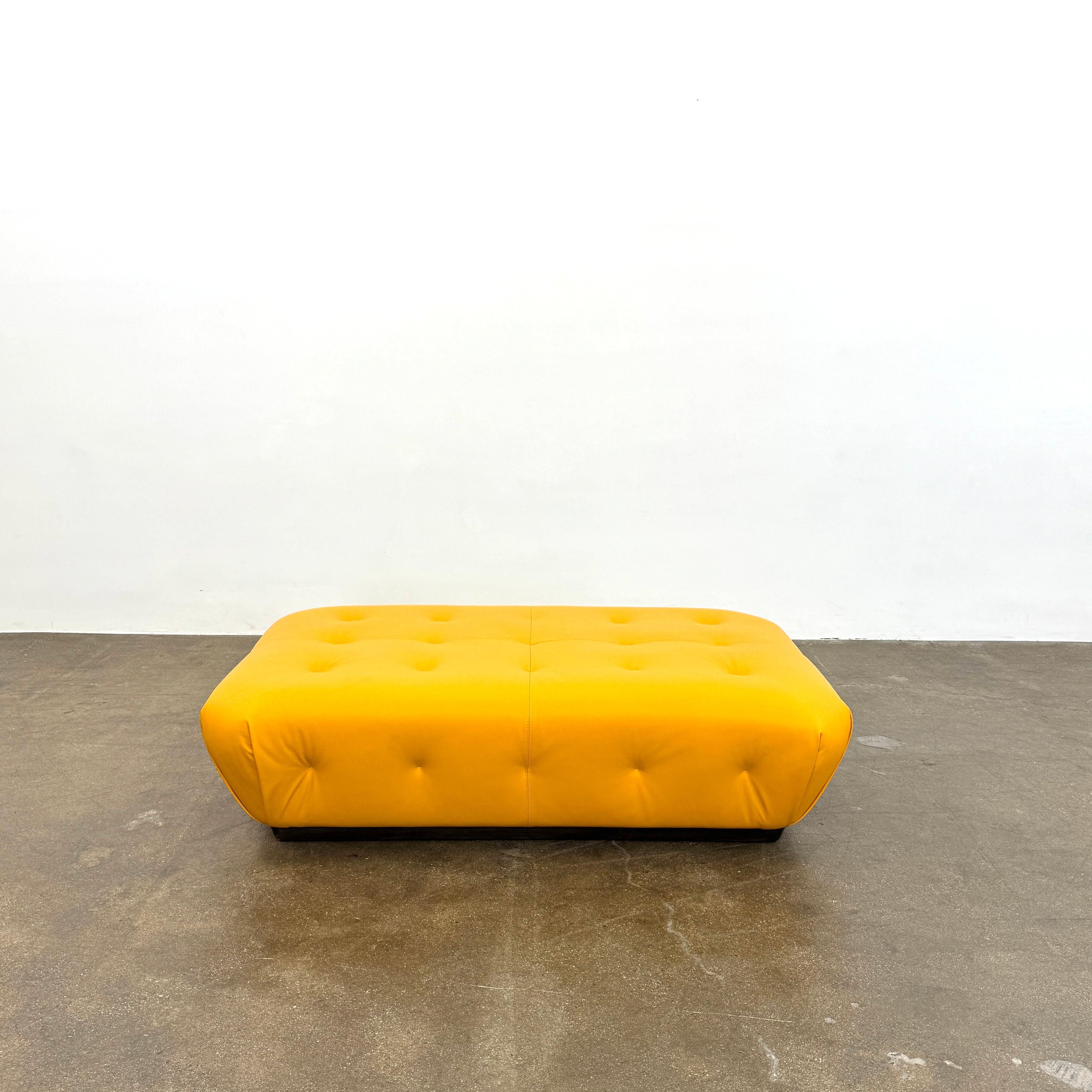 Yellow rectangular Tufted Leather Ottoman with rounded edges and a flat black base, ideal for extra seating, displayed on a plain white background. Brand: Unknown.