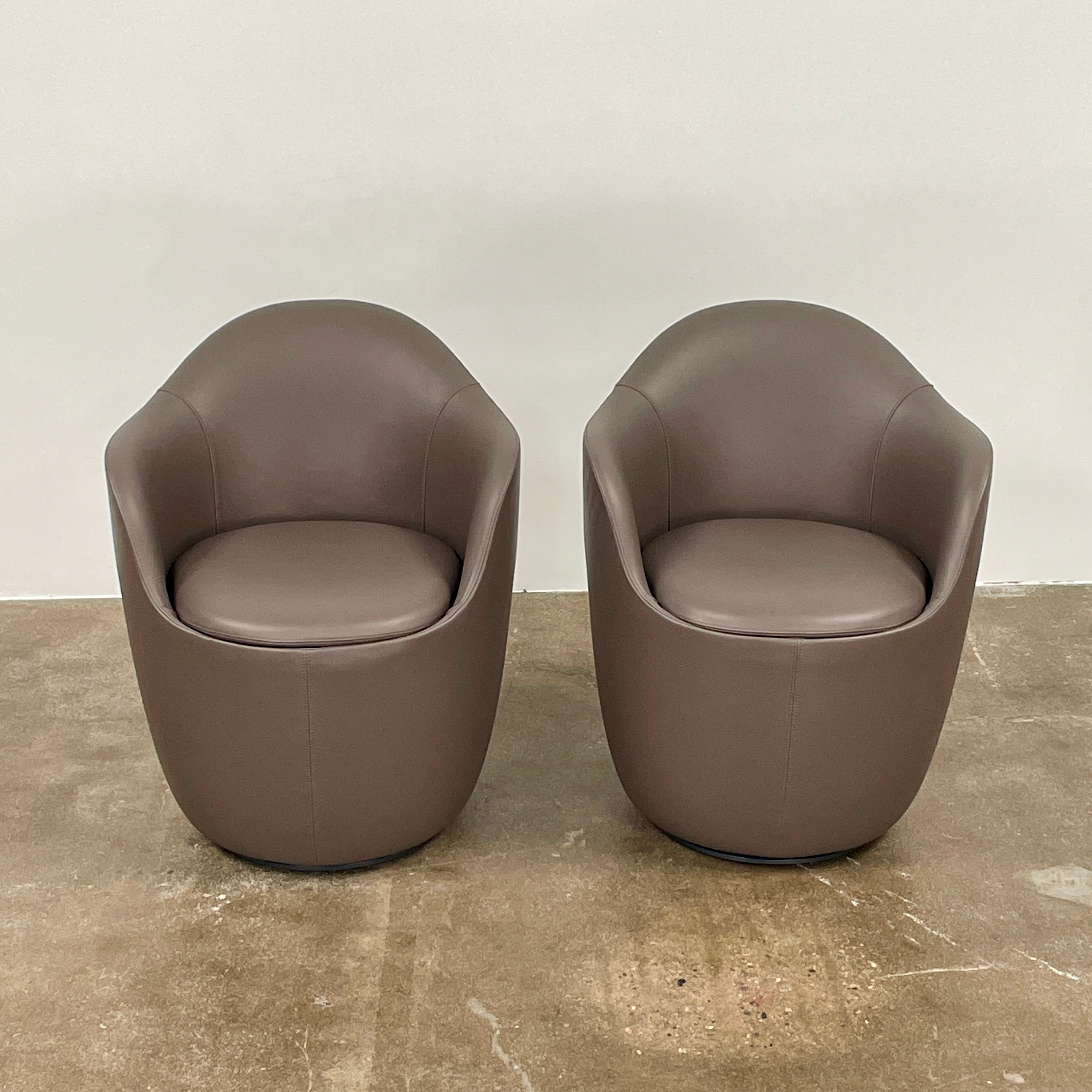 Two modern brown DWR Lina Swivel Dining Chairs with rounded backs and smooth upholstery, placed side by side on a white background.