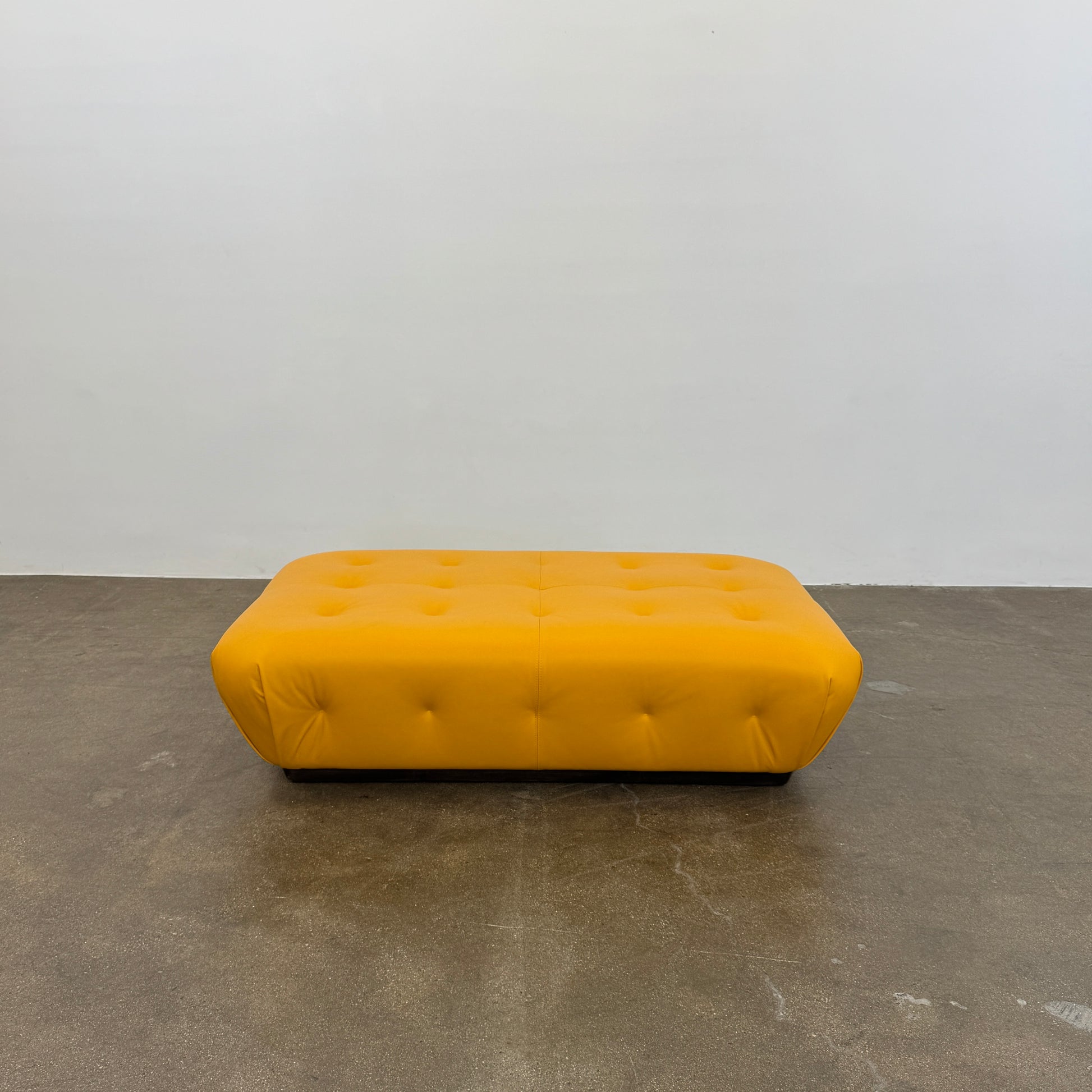 Yellow rectangular Tufted Leather Ottoman with rounded edges and a flat black base, ideal for extra seating, displayed on a plain white background. Brand: Unknown.