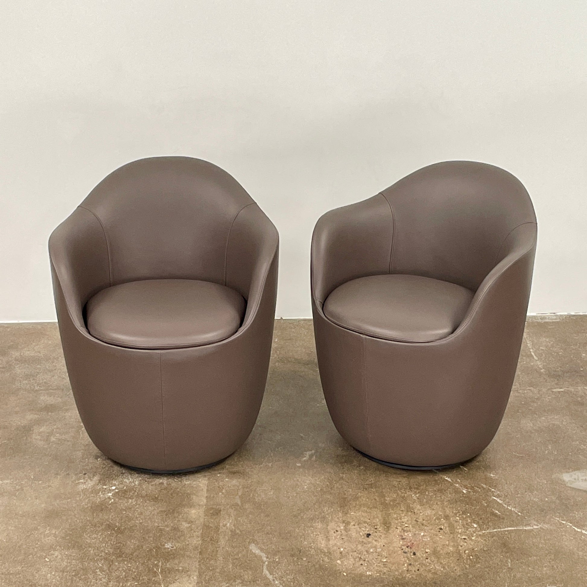 Two modern brown DWR Lina Swivel Dining Chairs with rounded backs and smooth upholstery, placed side by side on a white background.
