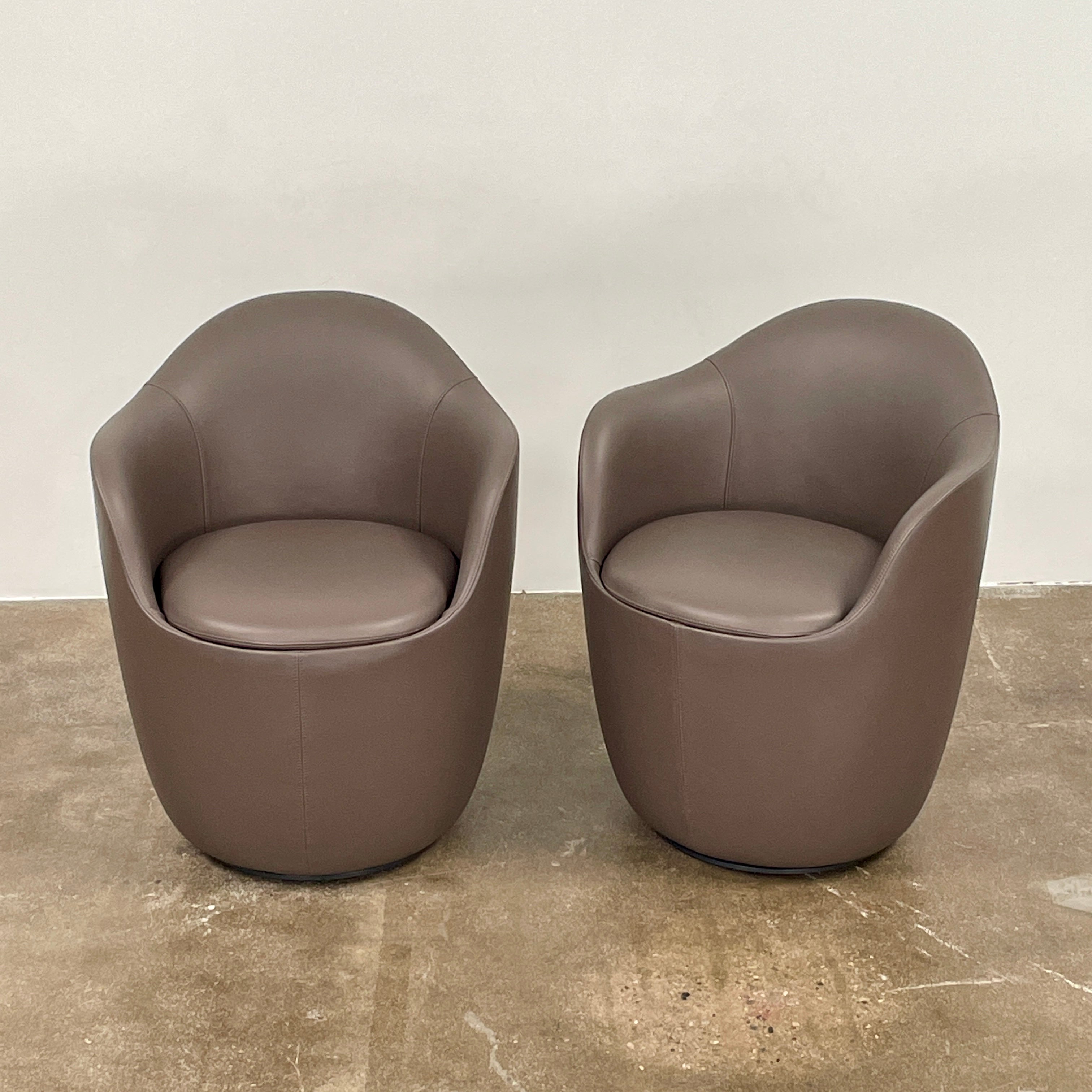 Two modern brown DWR Lina Swivel Dining Chairs with rounded backs and smooth upholstery, placed side by side on a white background.
