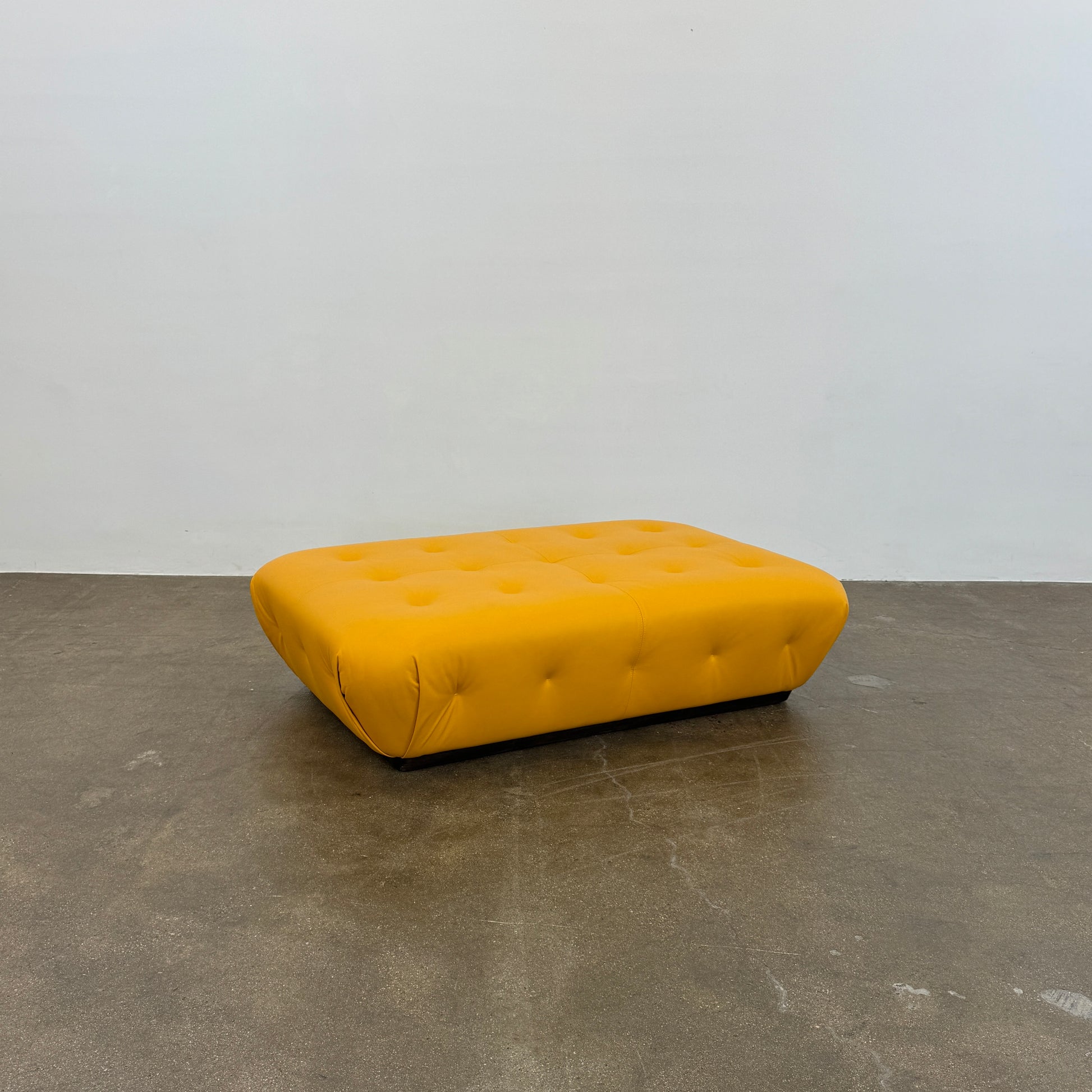 Yellow rectangular Tufted Leather Ottoman with rounded edges and a flat black base, ideal for extra seating, displayed on a plain white background. Brand: Unknown.