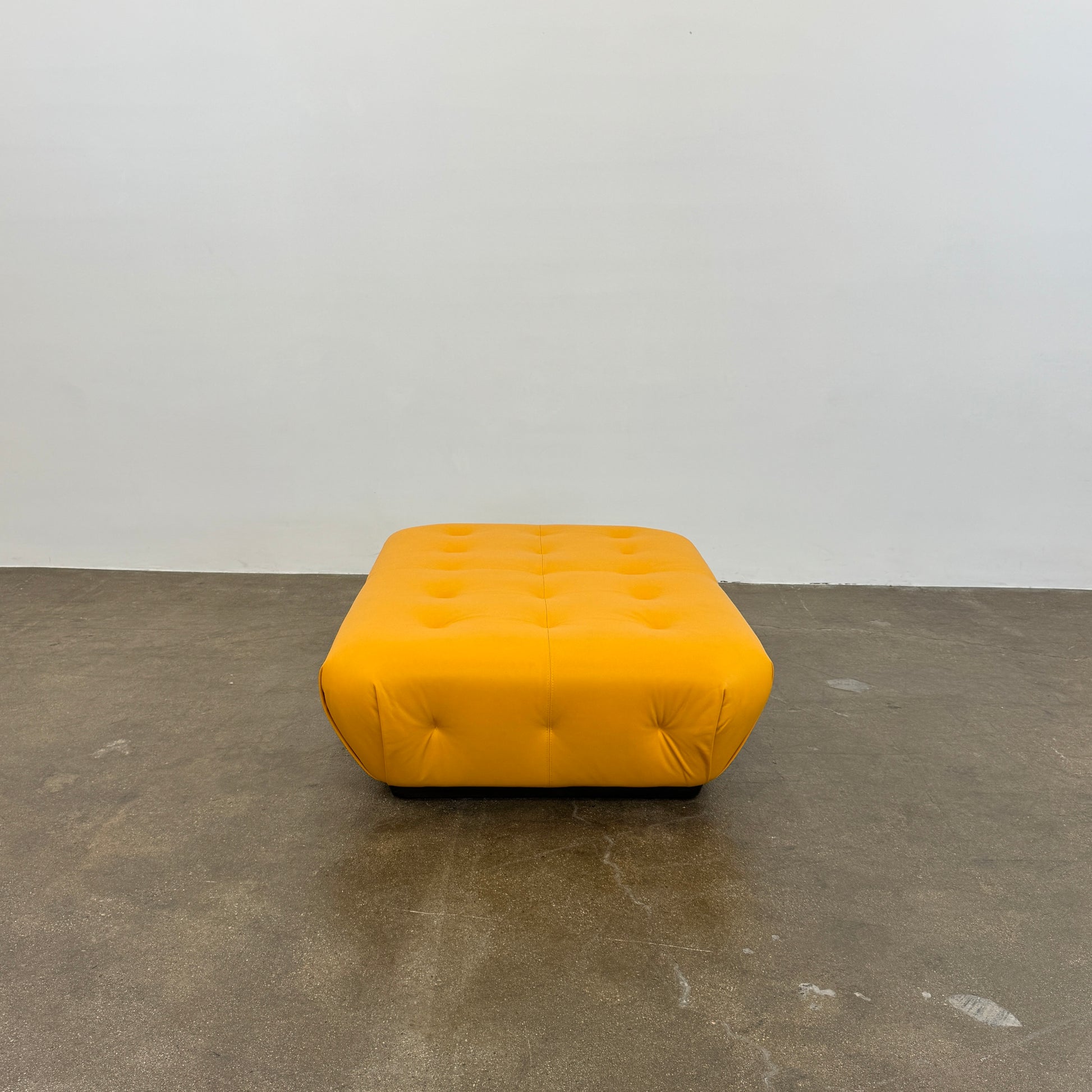 Yellow rectangular Tufted Leather Ottoman with rounded edges and a flat black base, ideal for extra seating, displayed on a plain white background. Brand: Unknown.