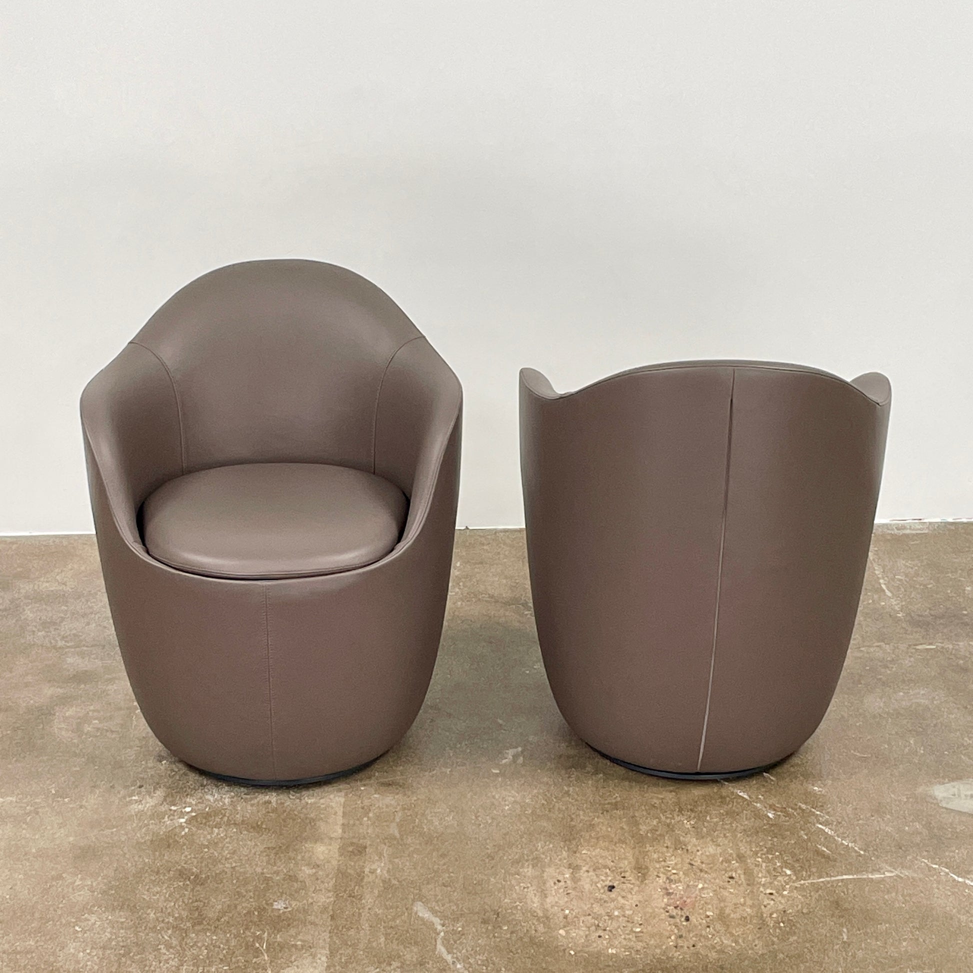 Two modern brown DWR Lina Swivel Dining Chairs with rounded backs and smooth upholstery, placed side by side on a white background.